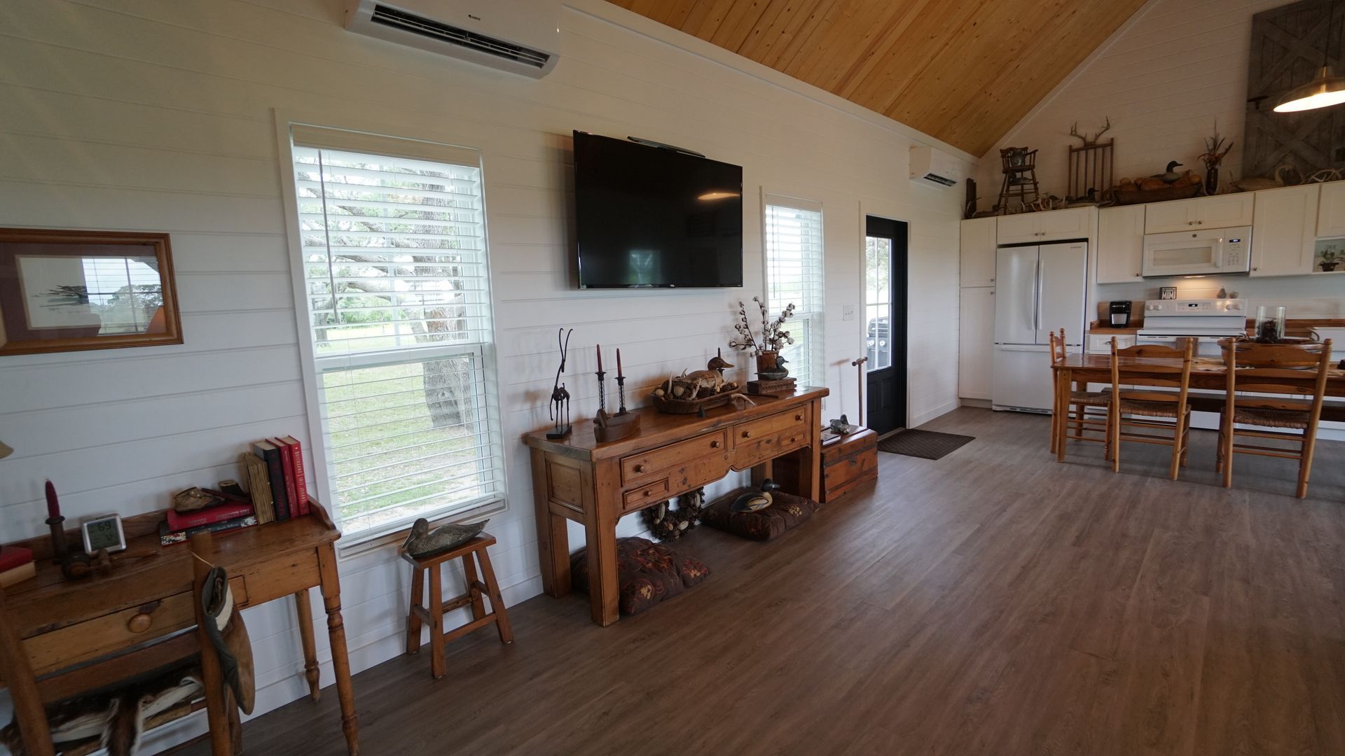 Interior of a house with wooden floors, white walls, and a wooden ceiling. A tv is mounted on the wall over a wooden table.