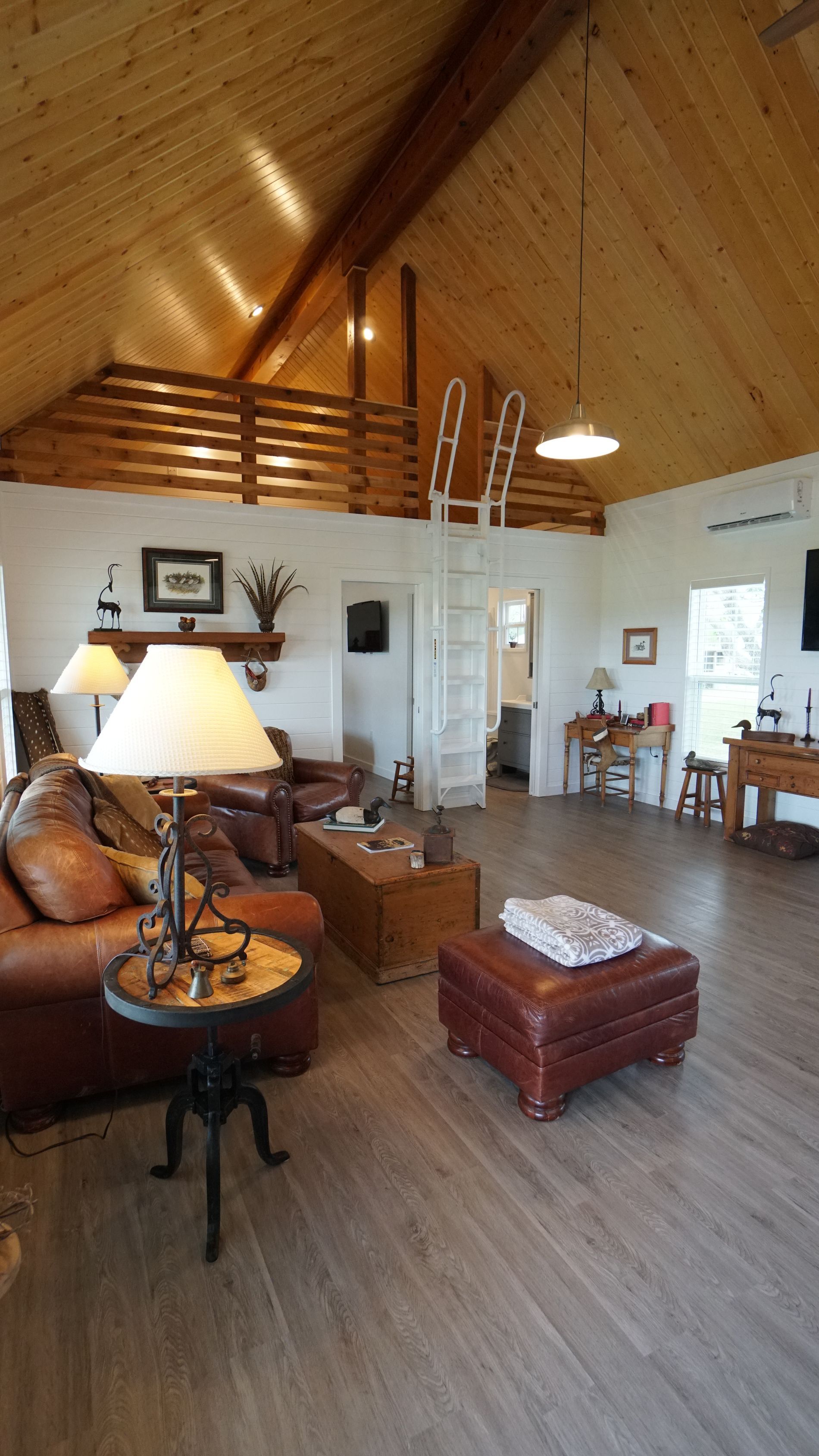 Living room with leather furniture, wood ceiling, white walls, and a ladder to a loft.