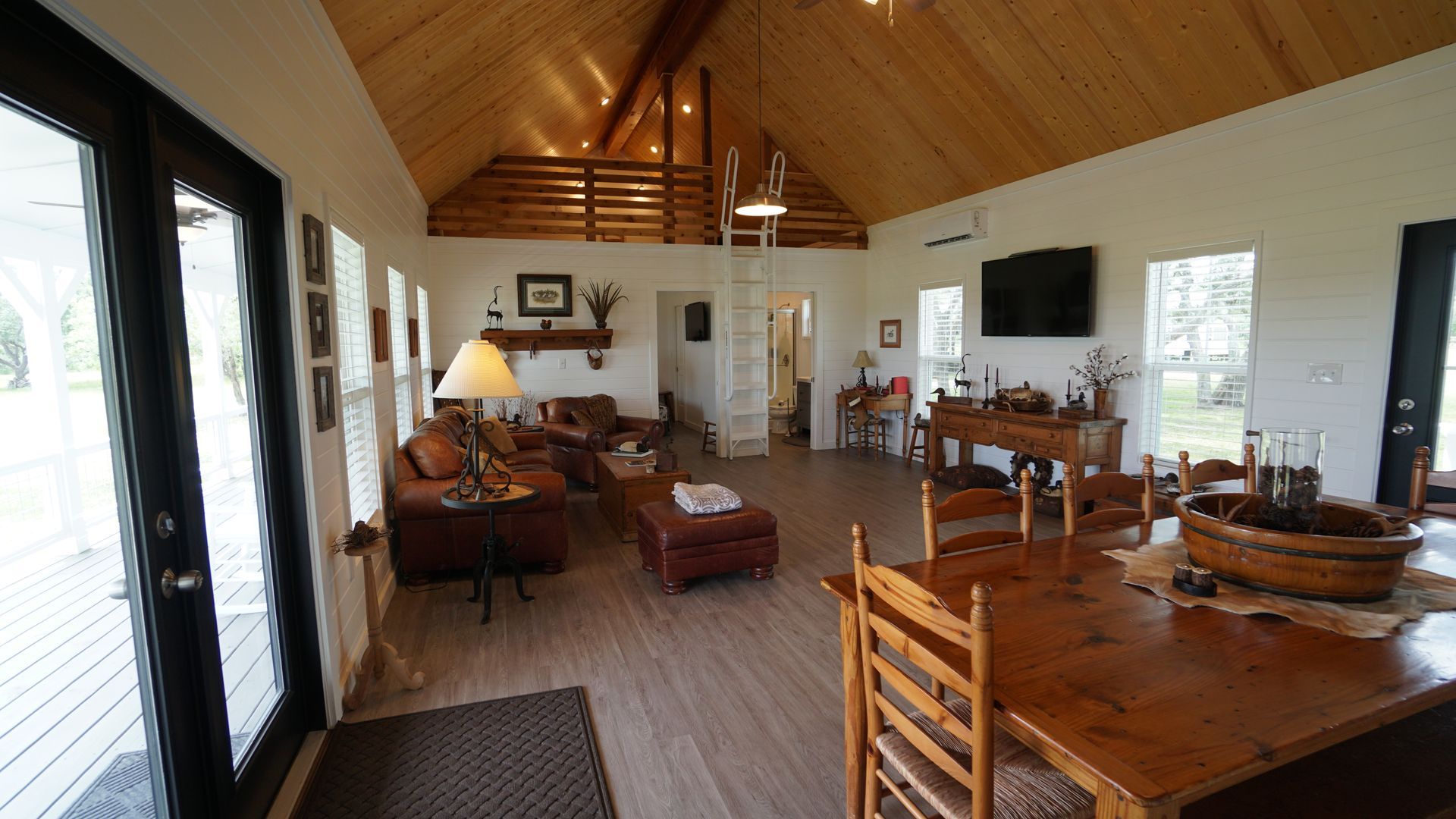 Spacious living area with wood ceiling and floors. Features seating, dining table, and ladder to loft.