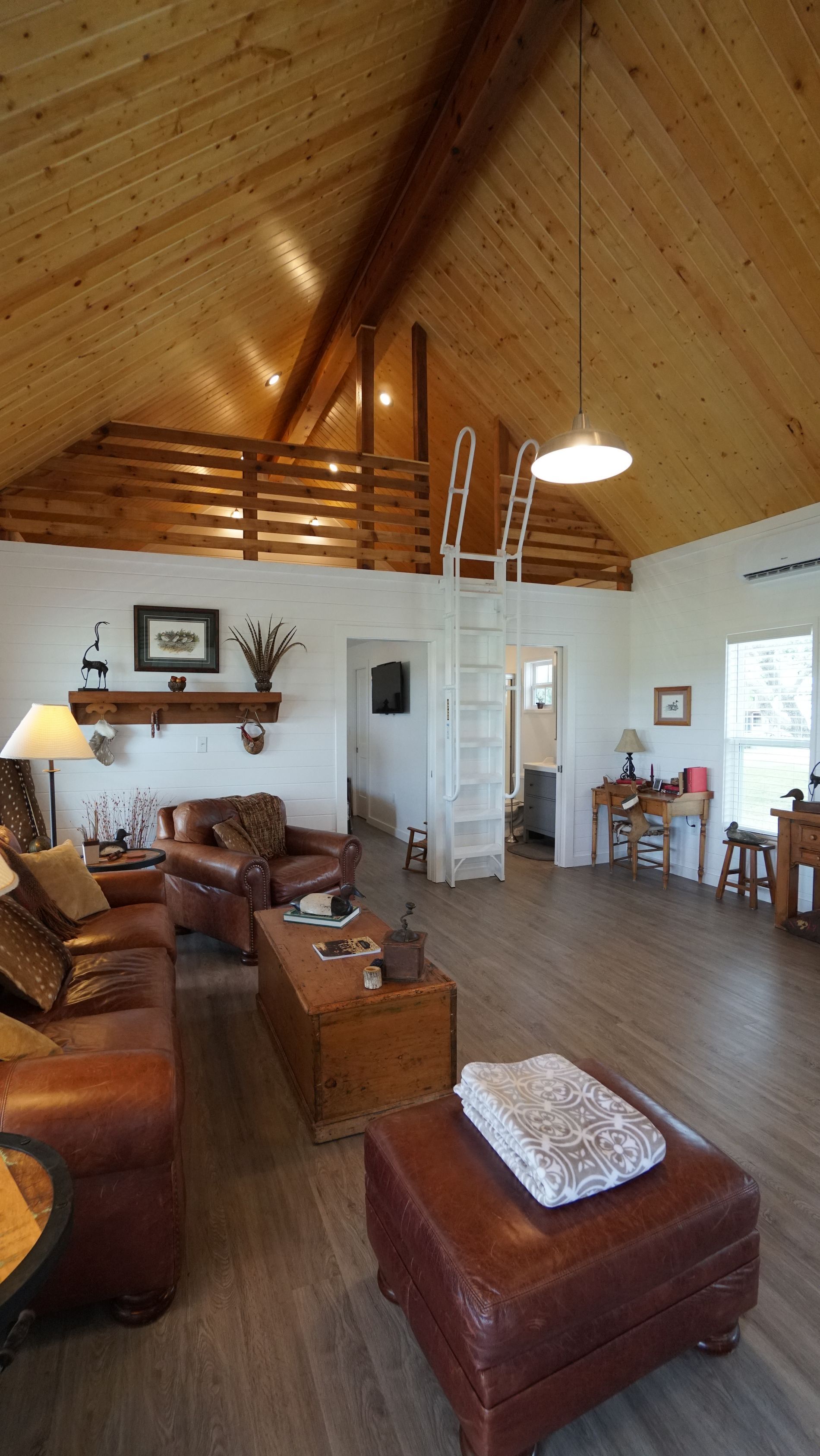 Living room with wood vaulted ceiling, leather furniture, and a ladder to a loft.