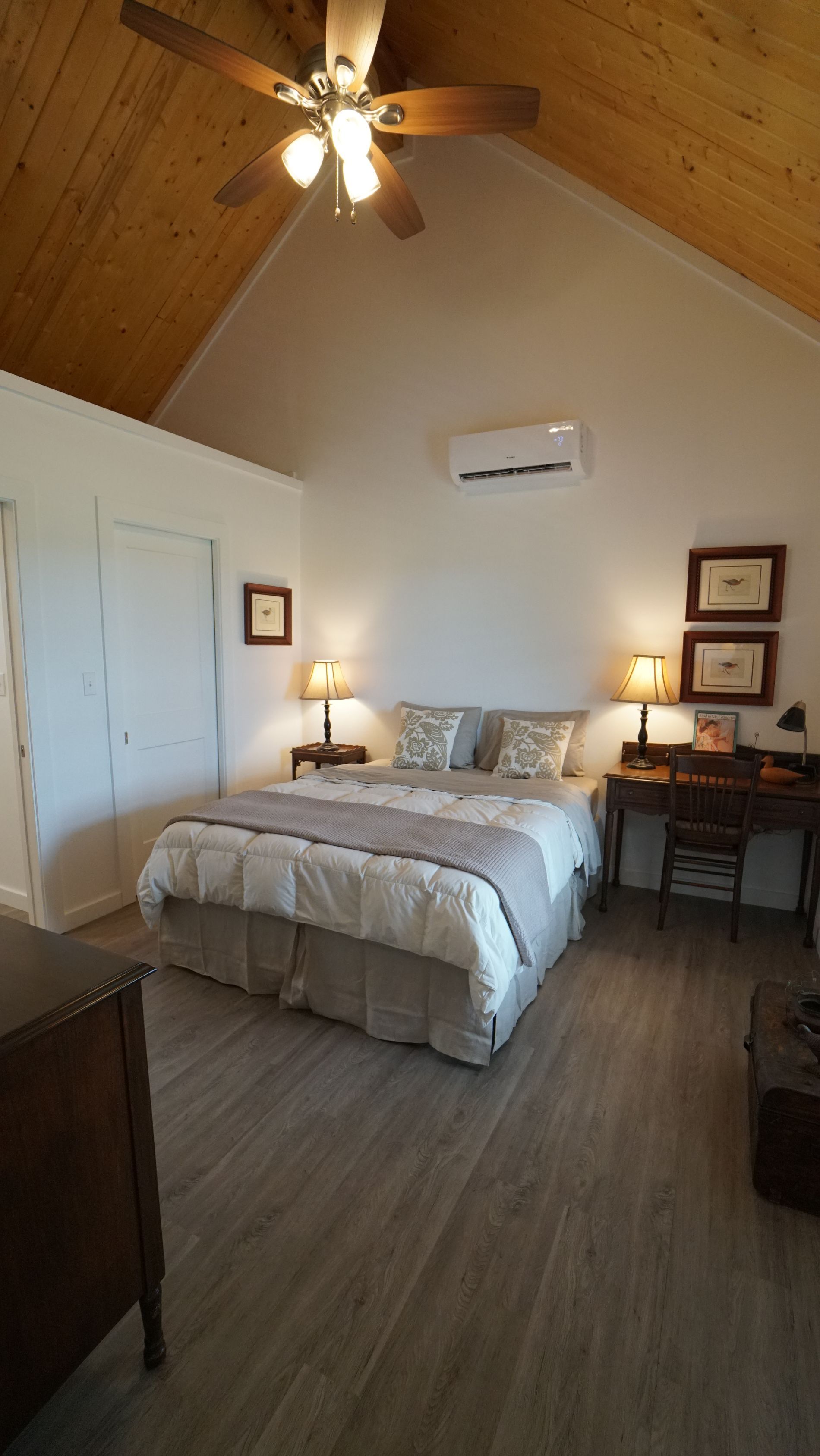 Bedroom with a bed, desk, and wood-paneled ceiling. White walls, a ceiling fan, and hardwood floors.