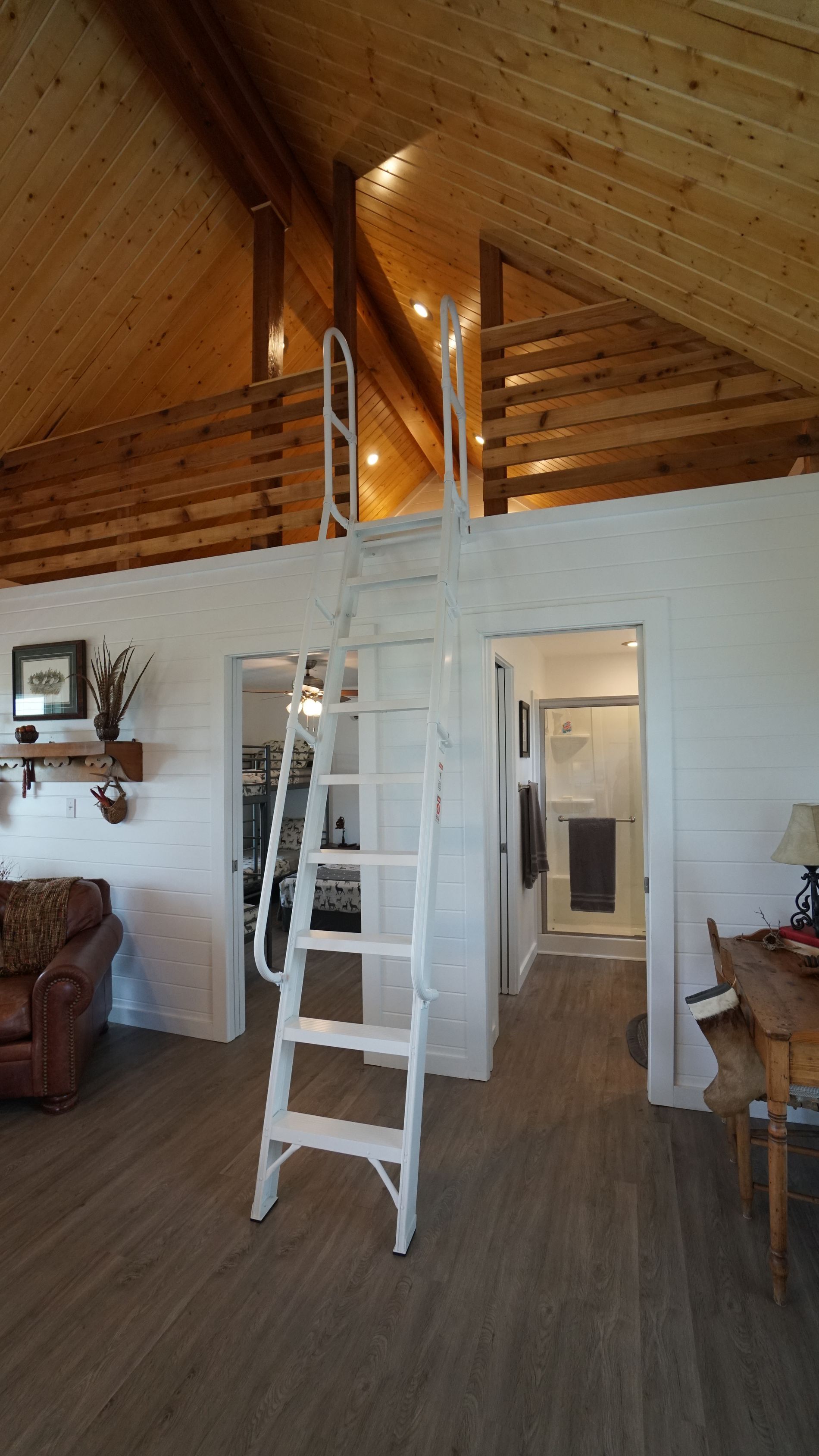White folding attic ladder in a home with wooden beams and a loft.
