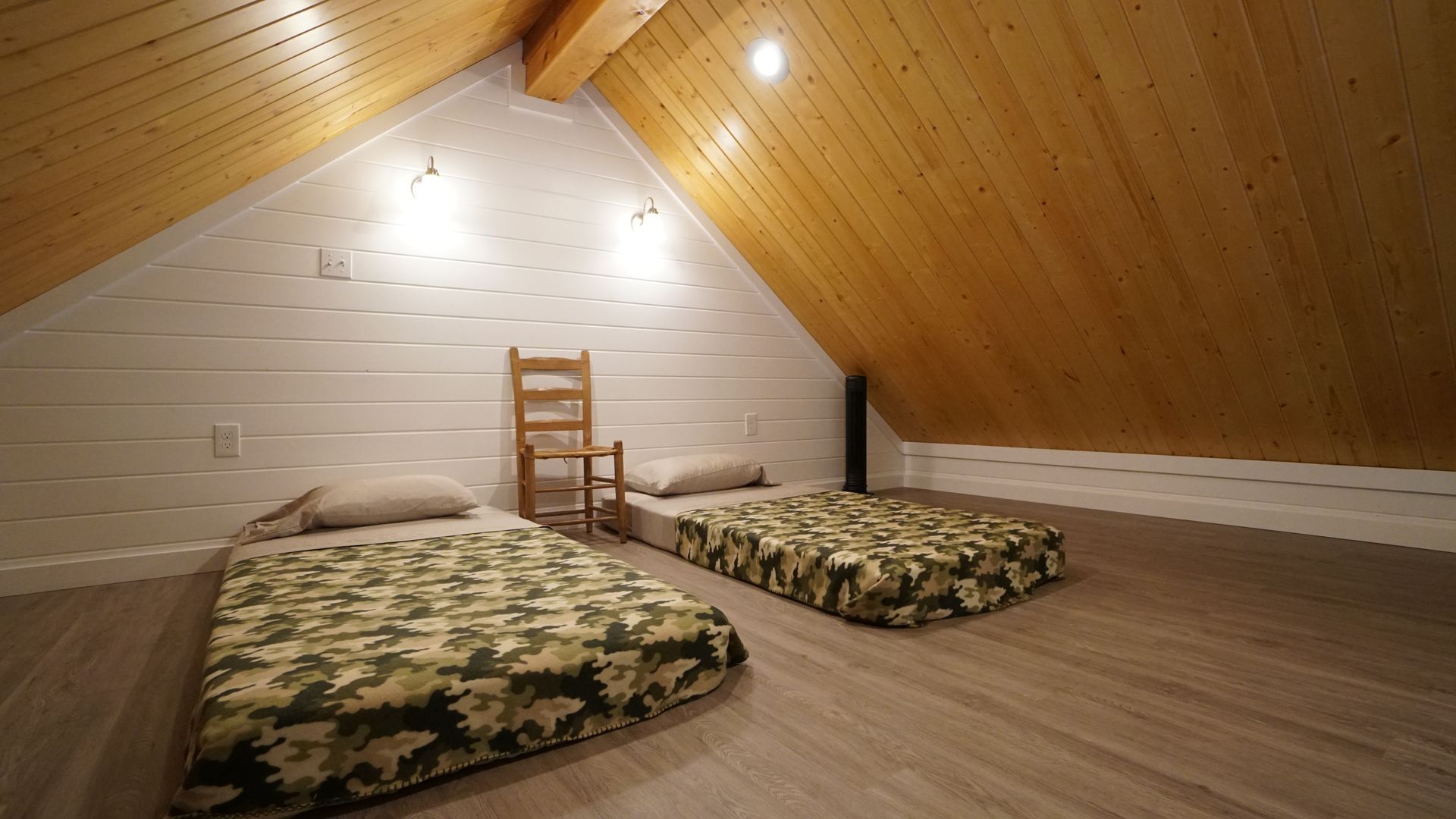 Attic bedroom with two floor mattresses, a wooden chair, wood ceiling and white walls.