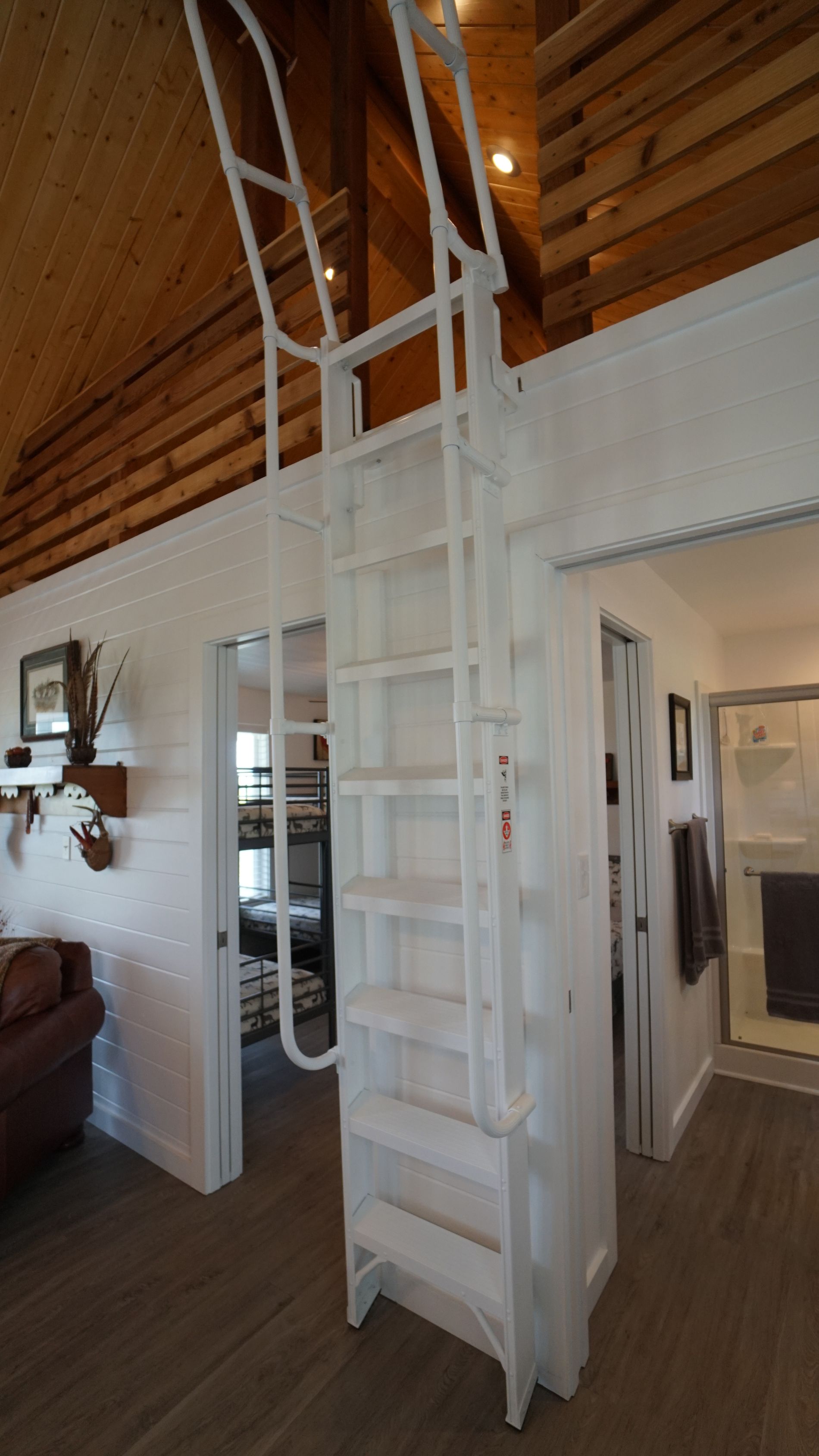 White enclosed ladder to a loft, in a room with wood ceiling and white walls.