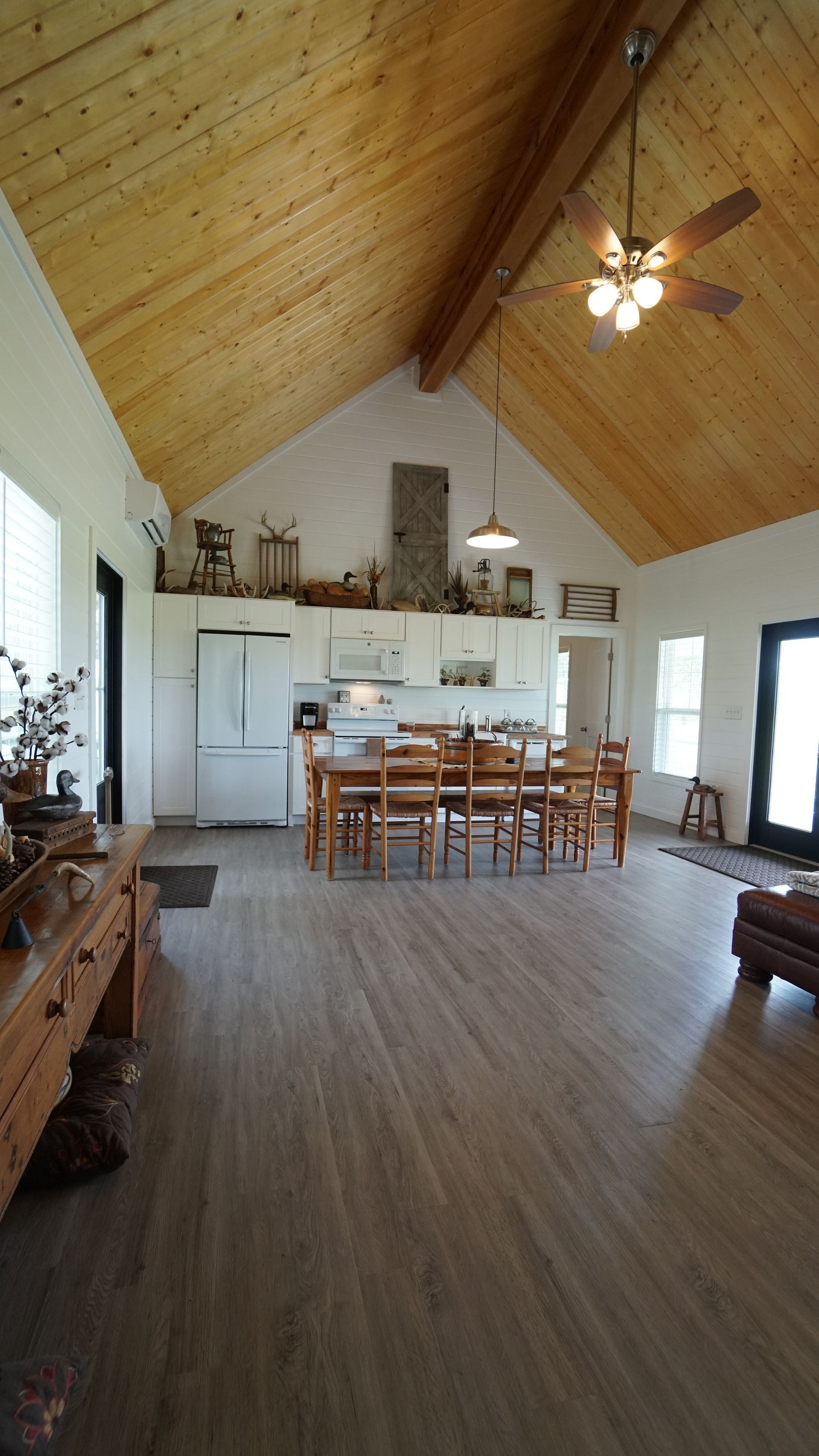 Open kitchen with wooden floors, vaulted wood ceiling, and a large dining table.