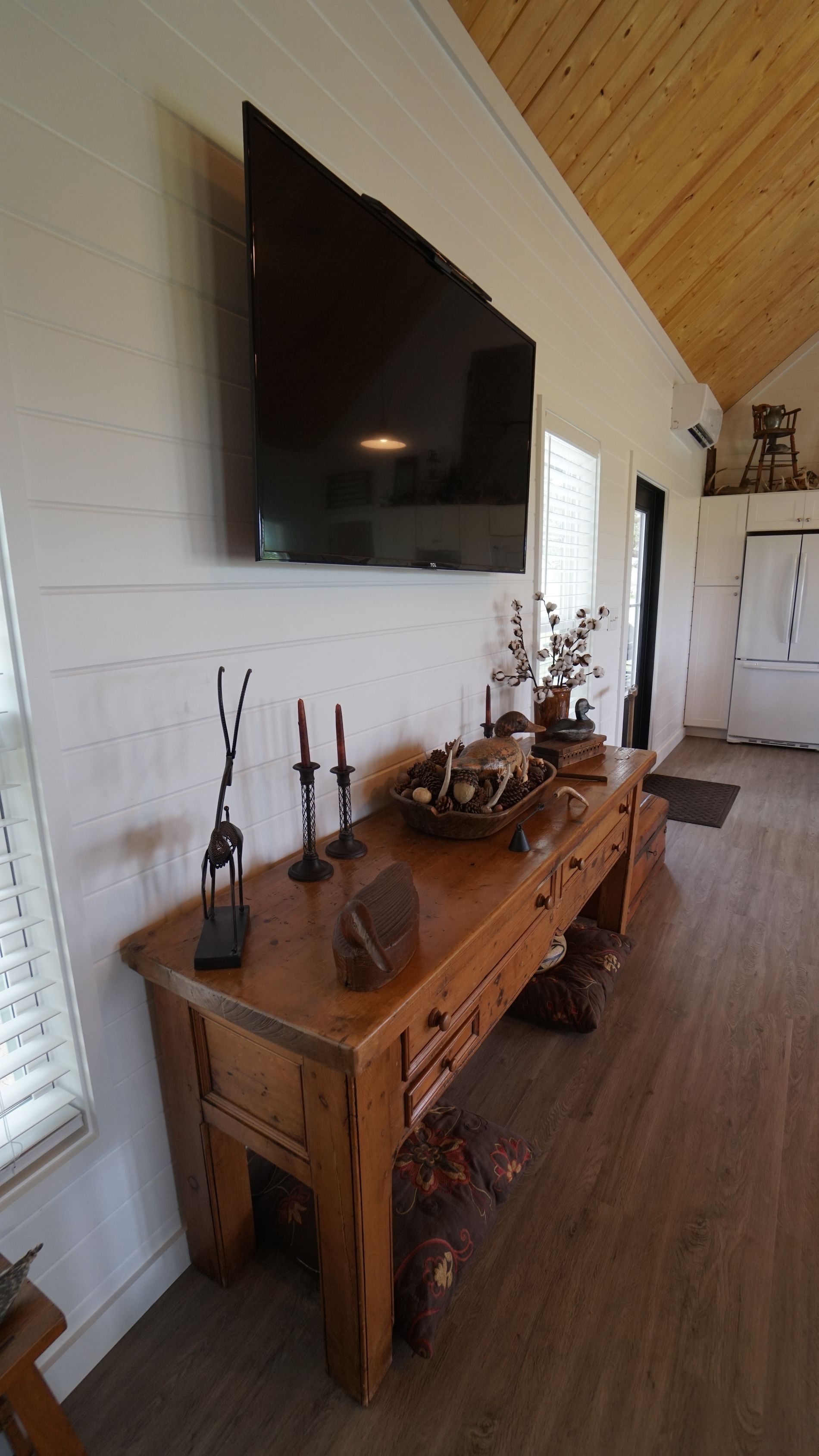 Wooden console table with decor beneath a mounted TV in a white-walled room.