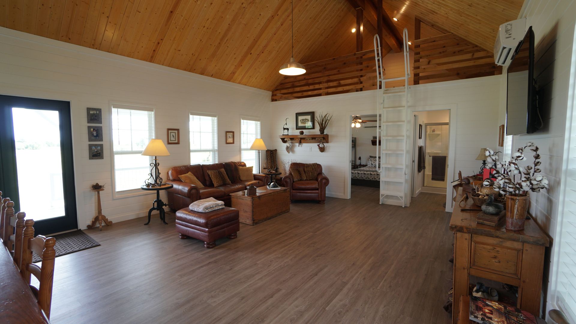 Spacious living room with wood ceiling, seating area, and a ladder leading upwards.