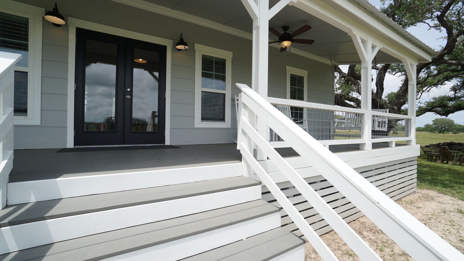 Gray and white house exterior with porch, stairs, and double doors.