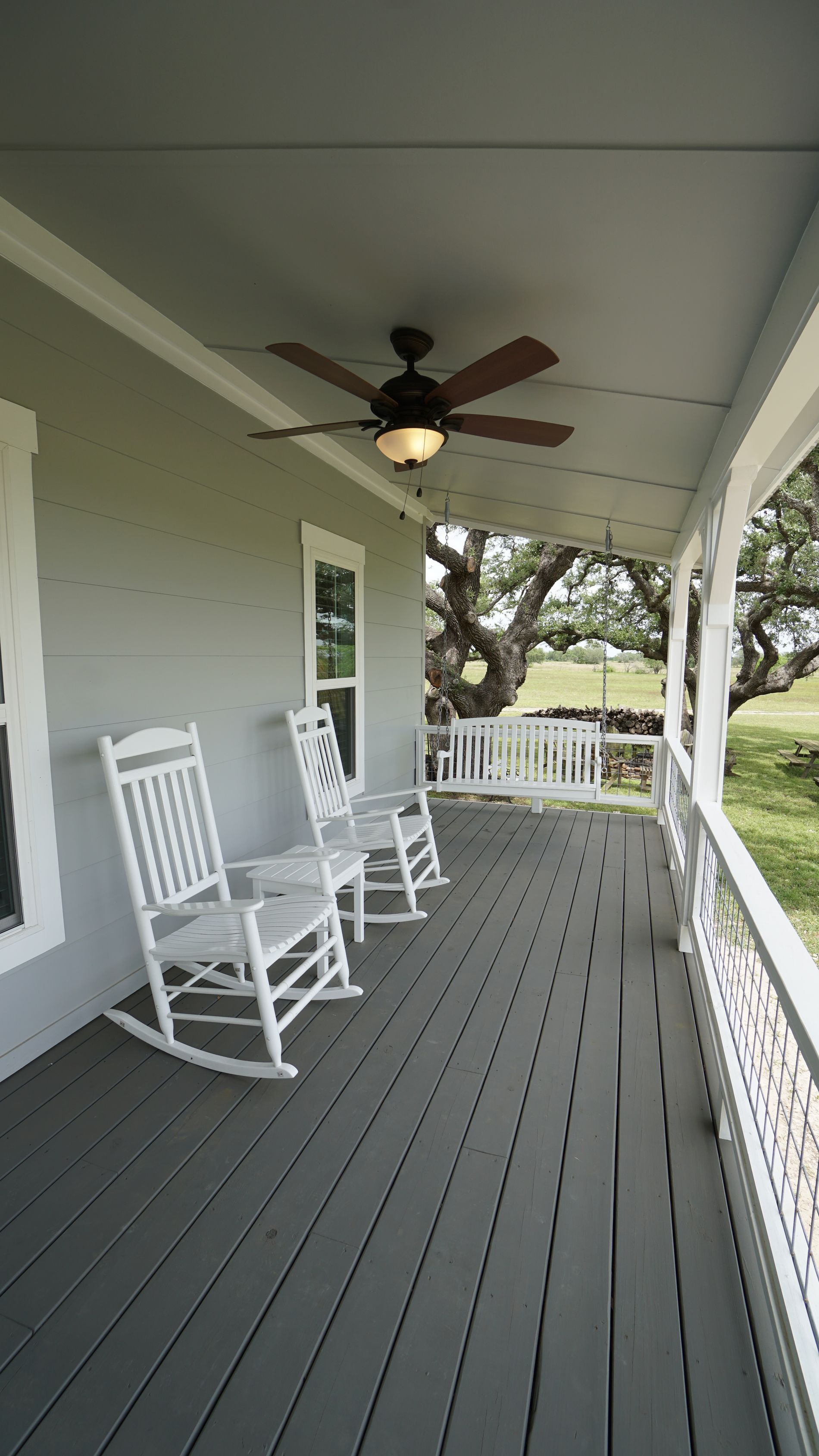 Porch with gray decking, white rocking chairs, and ceiling fan.