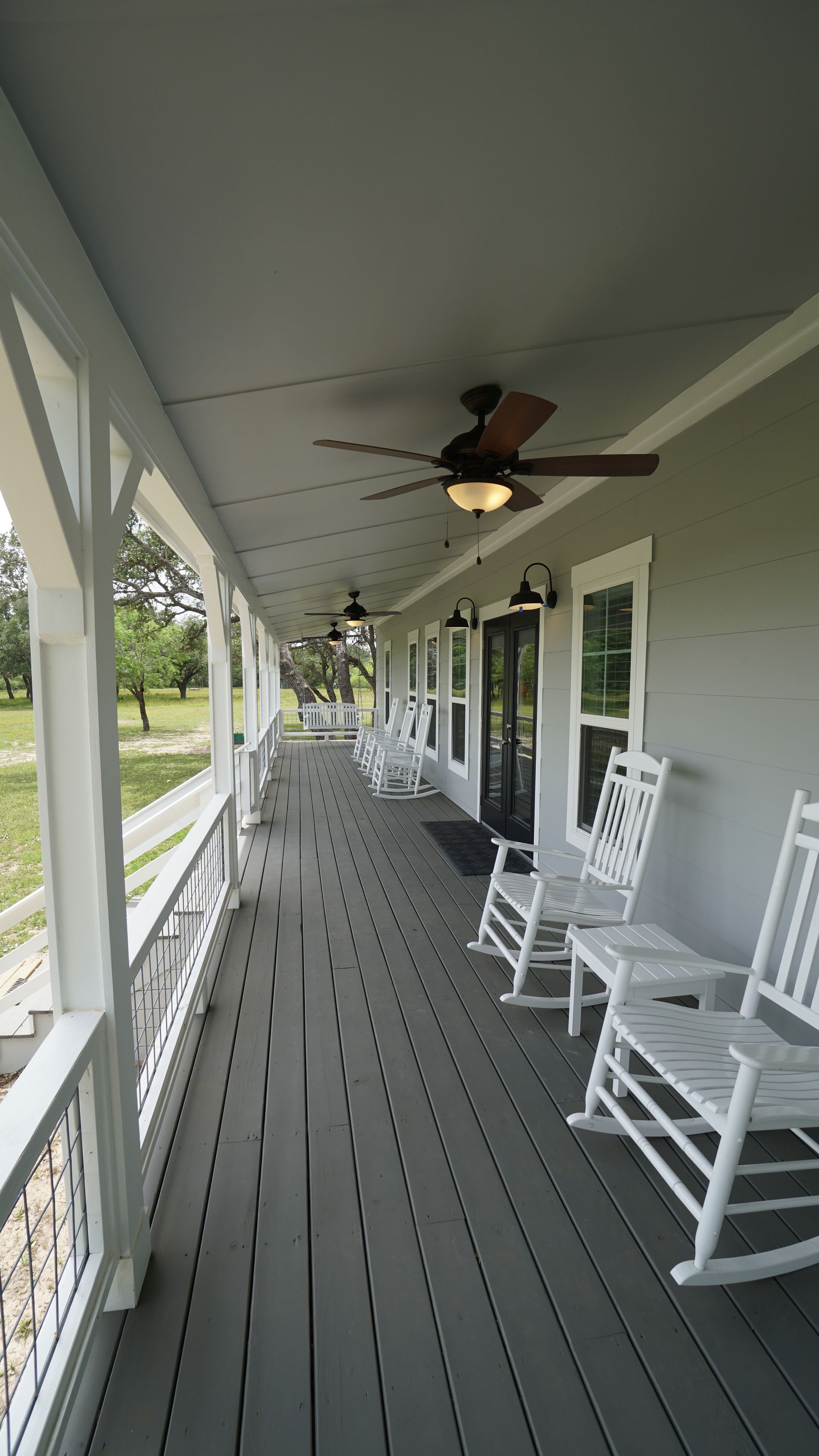 Long porch with white rocking chairs, gray floor, white railing and ceiling, black lights.