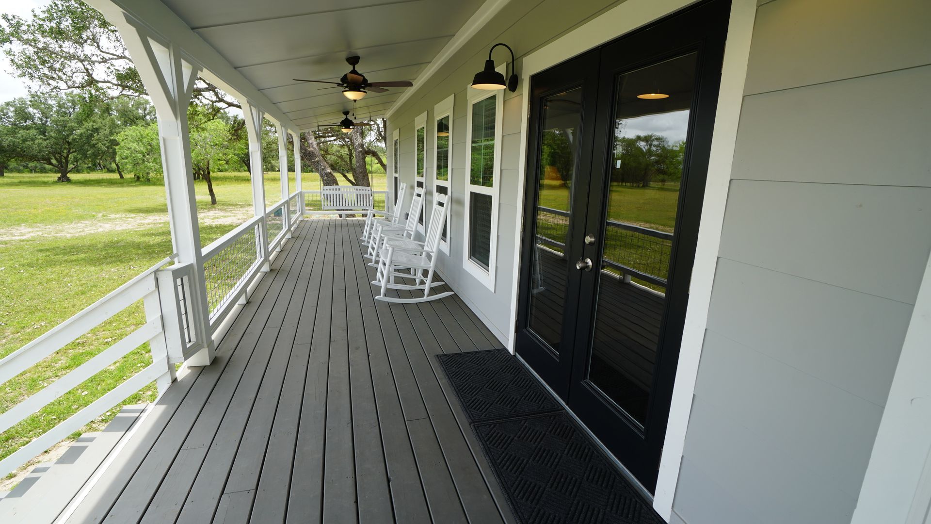 Gray porch with black door, white rocking chairs, and a green yard.