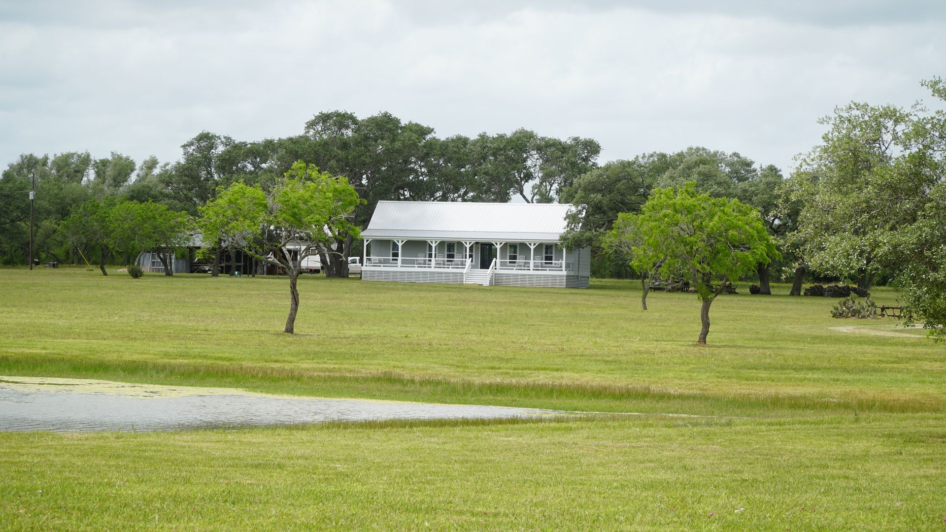White house with porch, set on a green grassy lawn with trees, under a cloudy sky.