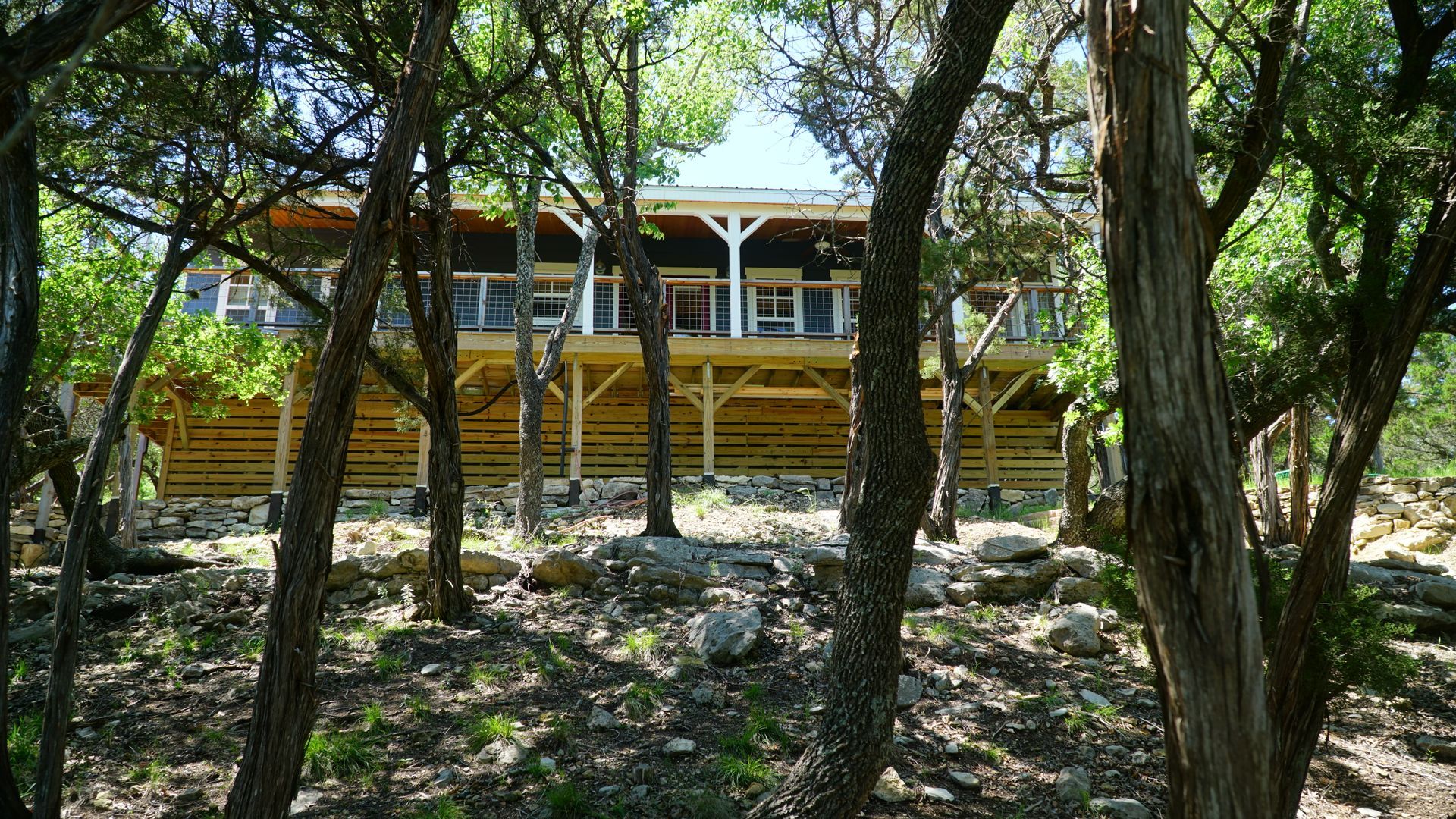 Wooden house on stilts in a forest, viewed through trees.