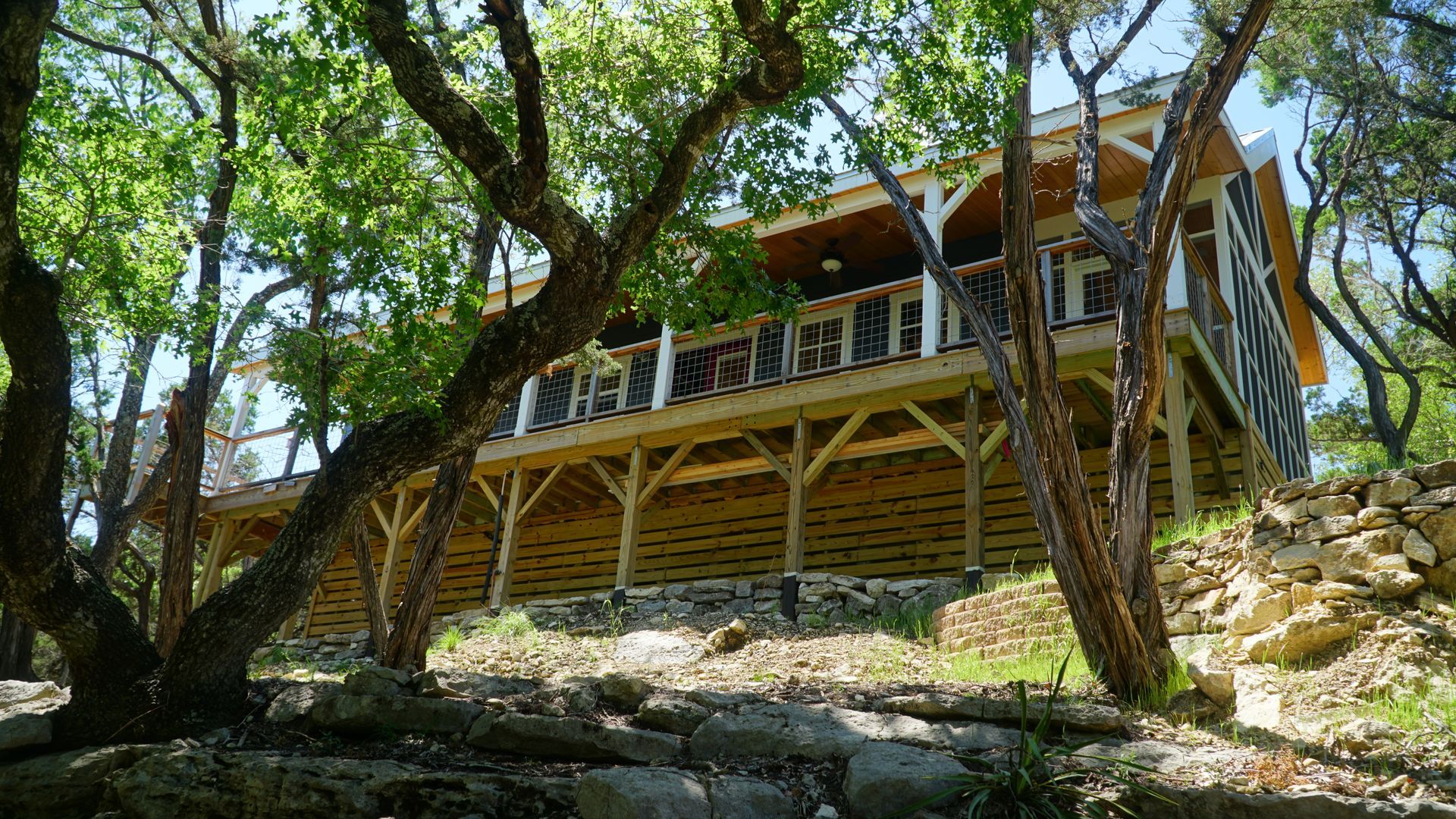 Wooden cabin in a wooded area with a large porch and stone base.