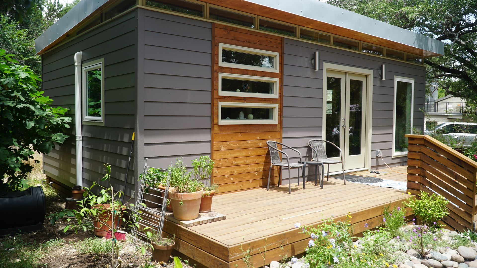 Tiny house with grey siding, wooden deck, and small garden.