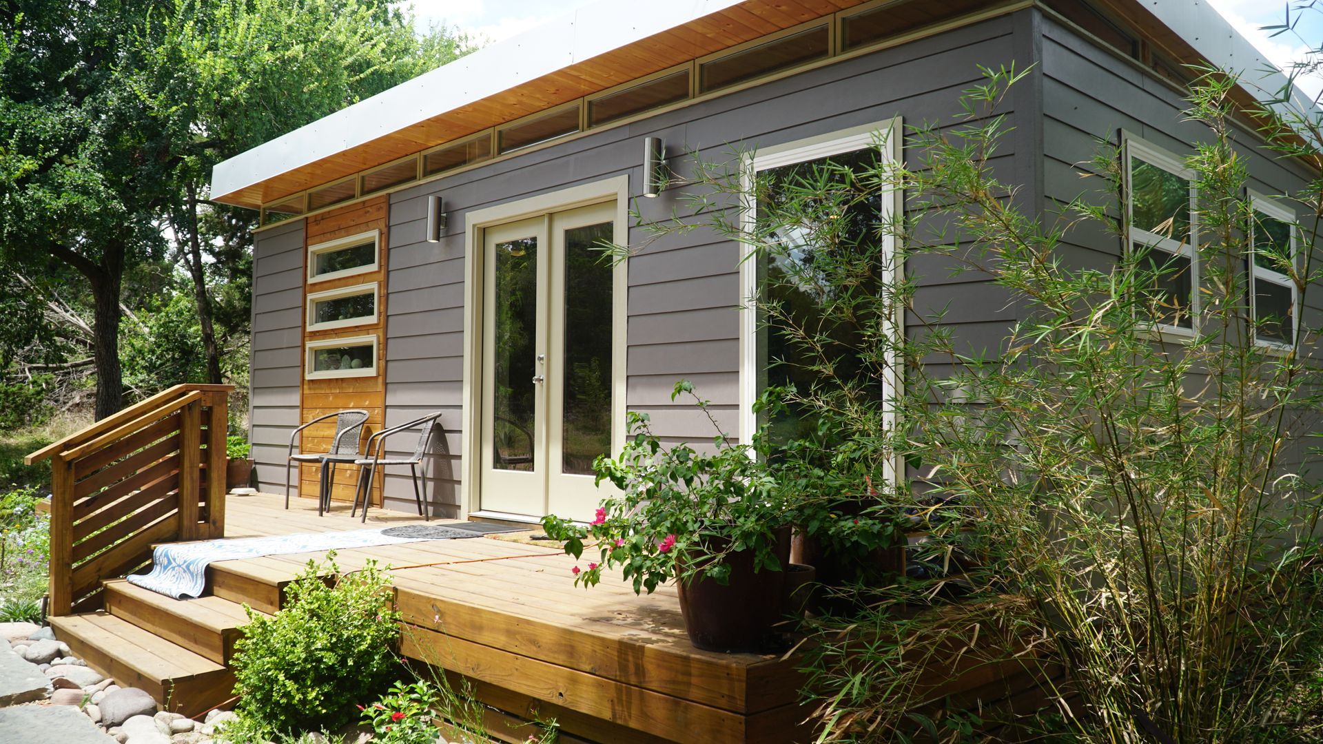Modern gray house with wooden deck, double doors, and potted plants.