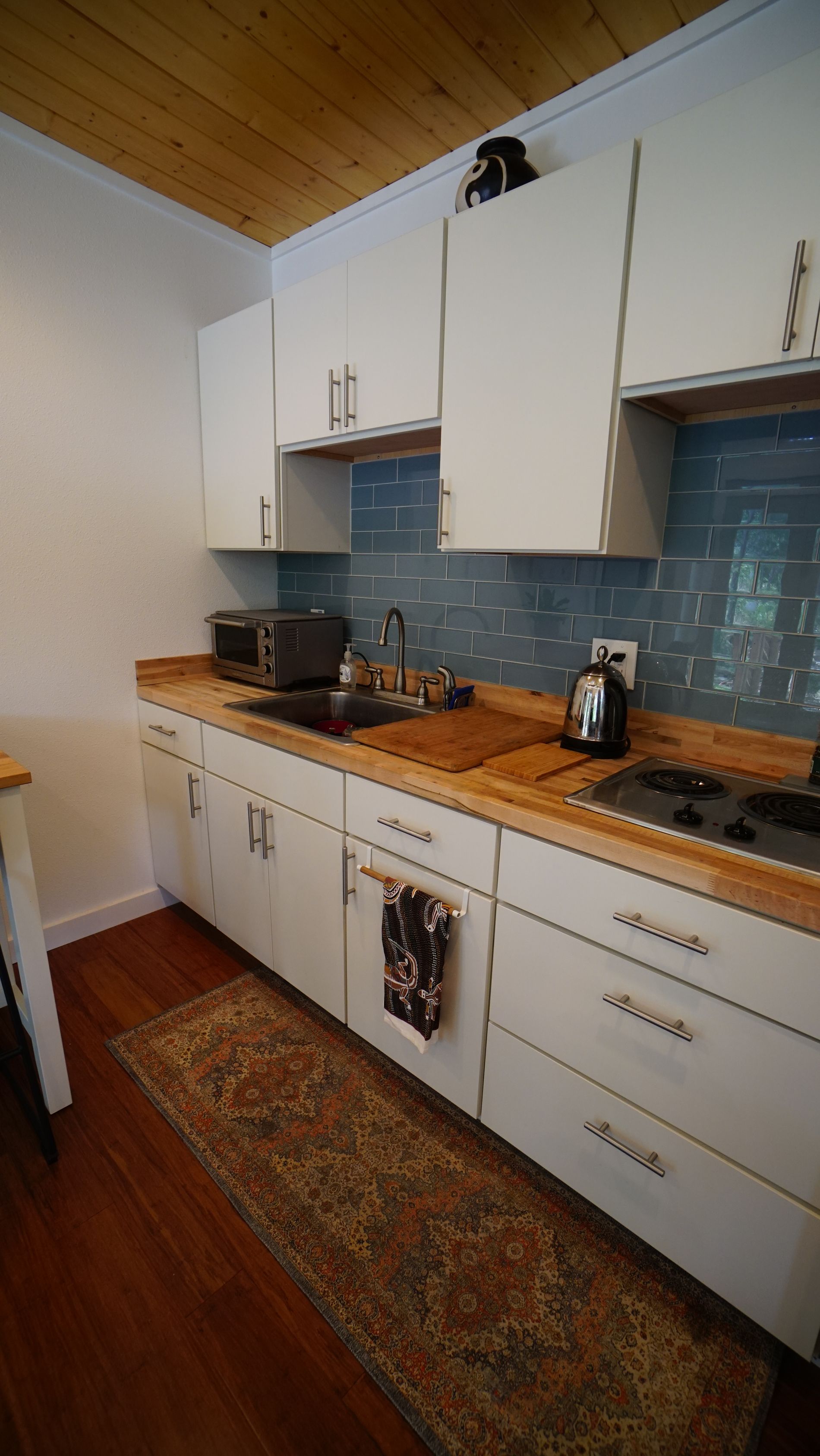 Small kitchen with white cabinets, wood countertop, blue backsplash, and area rug.