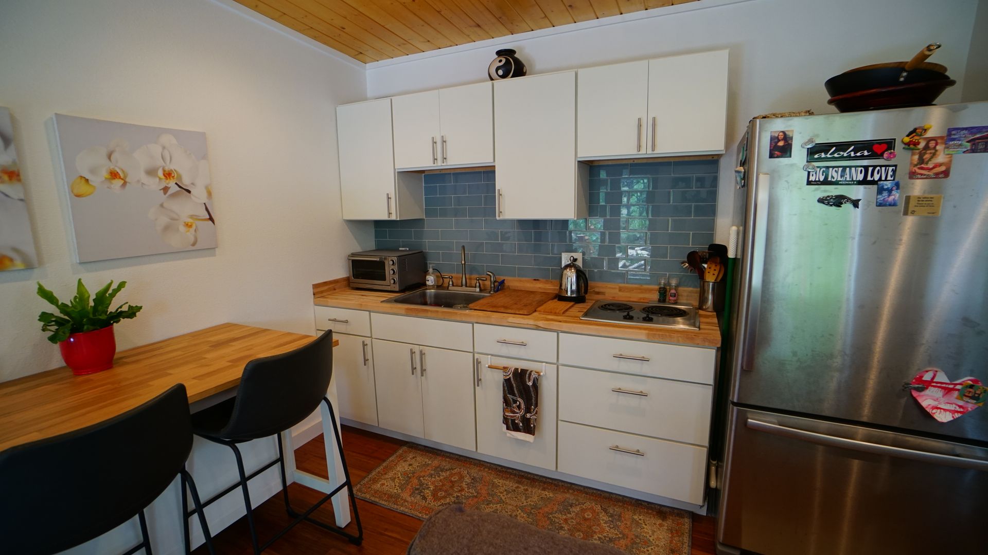 A small kitchen with white cabinets, a wooden countertop, and a stainless steel refrigerator.