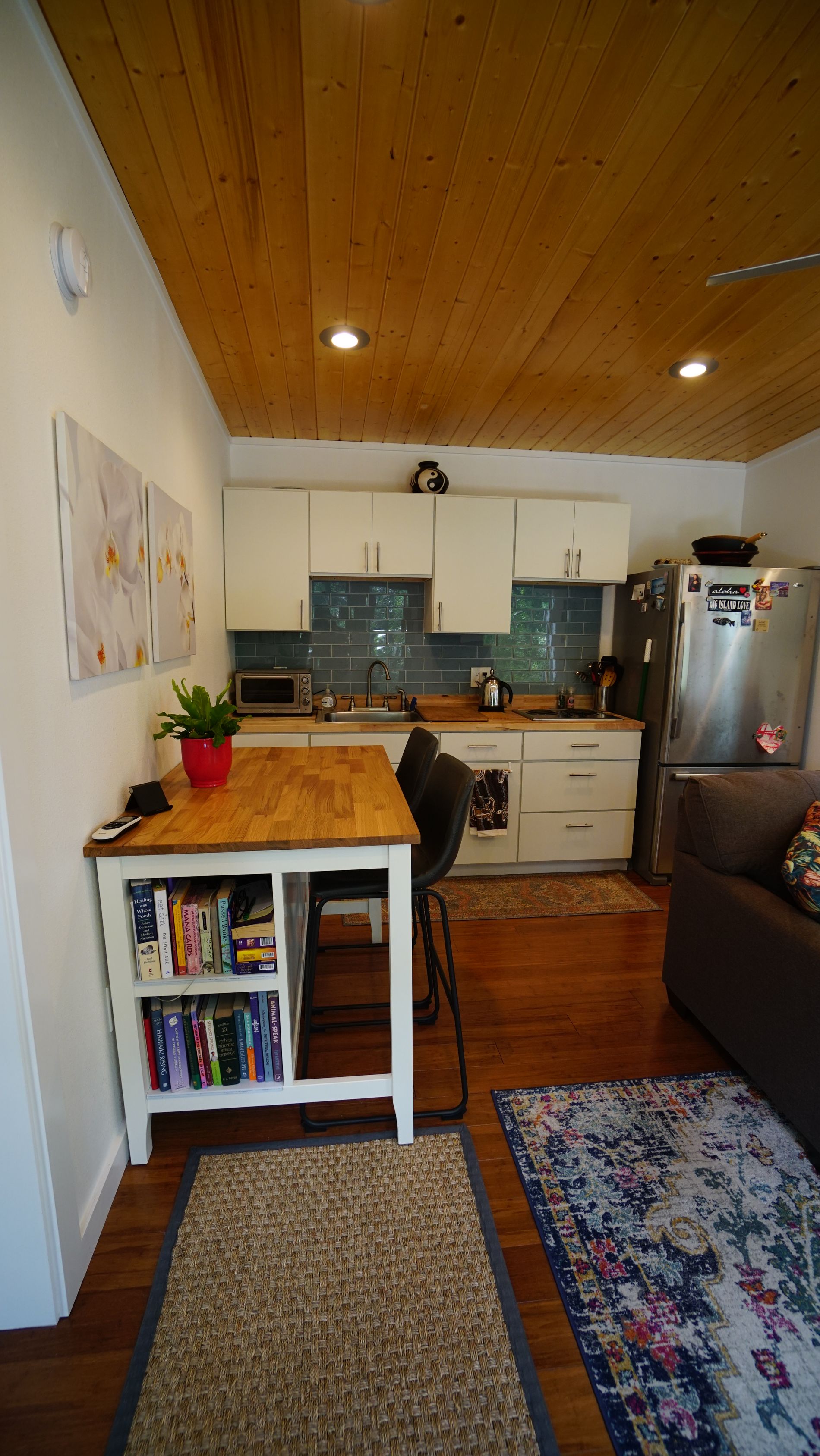 Small kitchen with wood ceiling, white cabinets, and a wooden table with books.