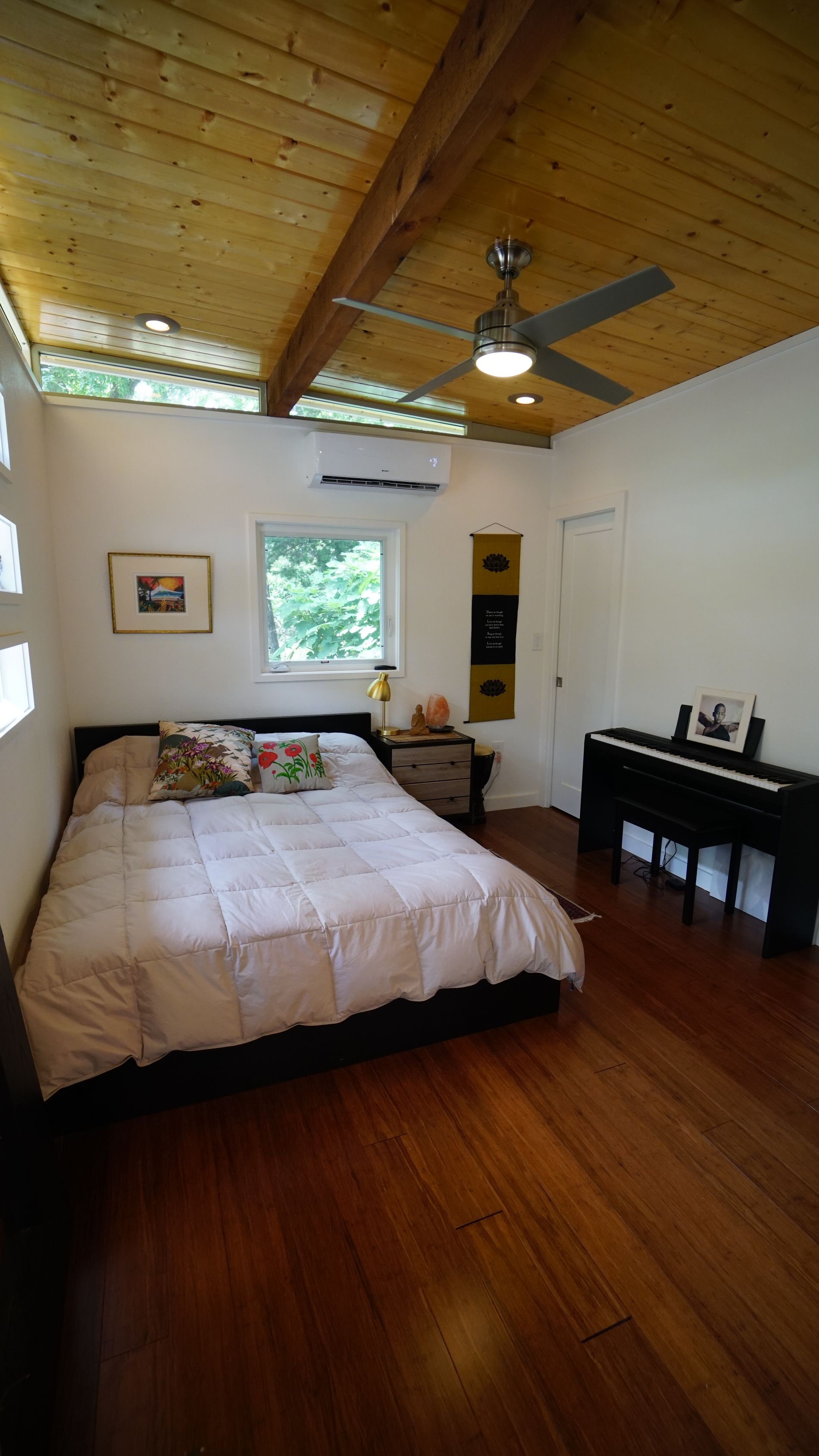 Bedroom with a bed, piano, and wooden ceiling. White walls, hardwood floor.