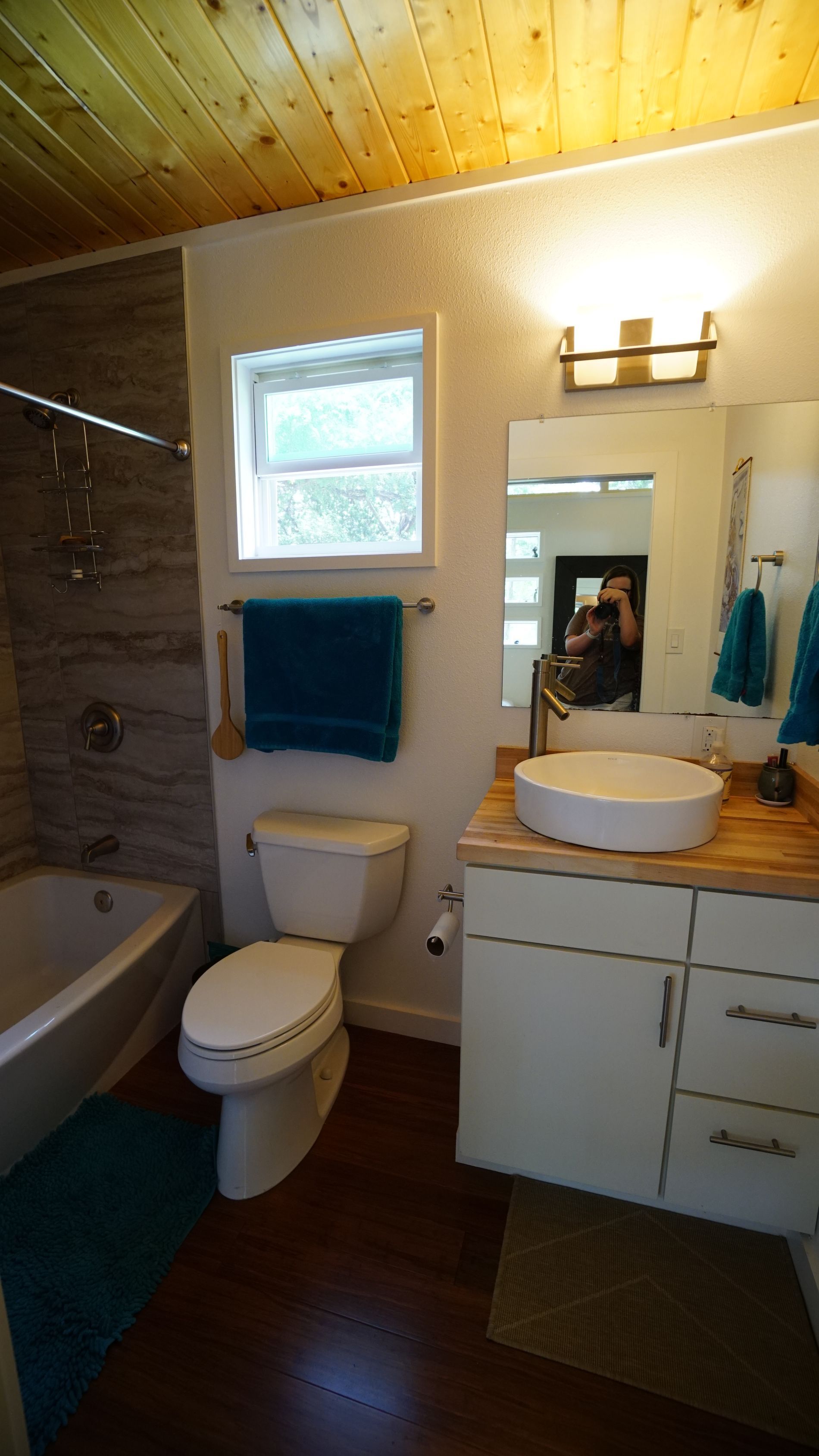 Bathroom with wood ceiling, white walls, and dark wood floor. Features include a tub, toilet, and vessel sink.