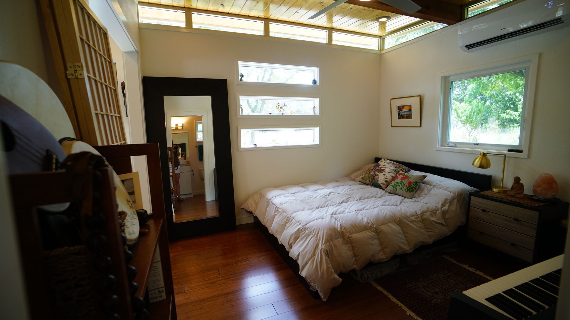 Bedroom with bed, mirror, and small window. Off-white walls, natural light.