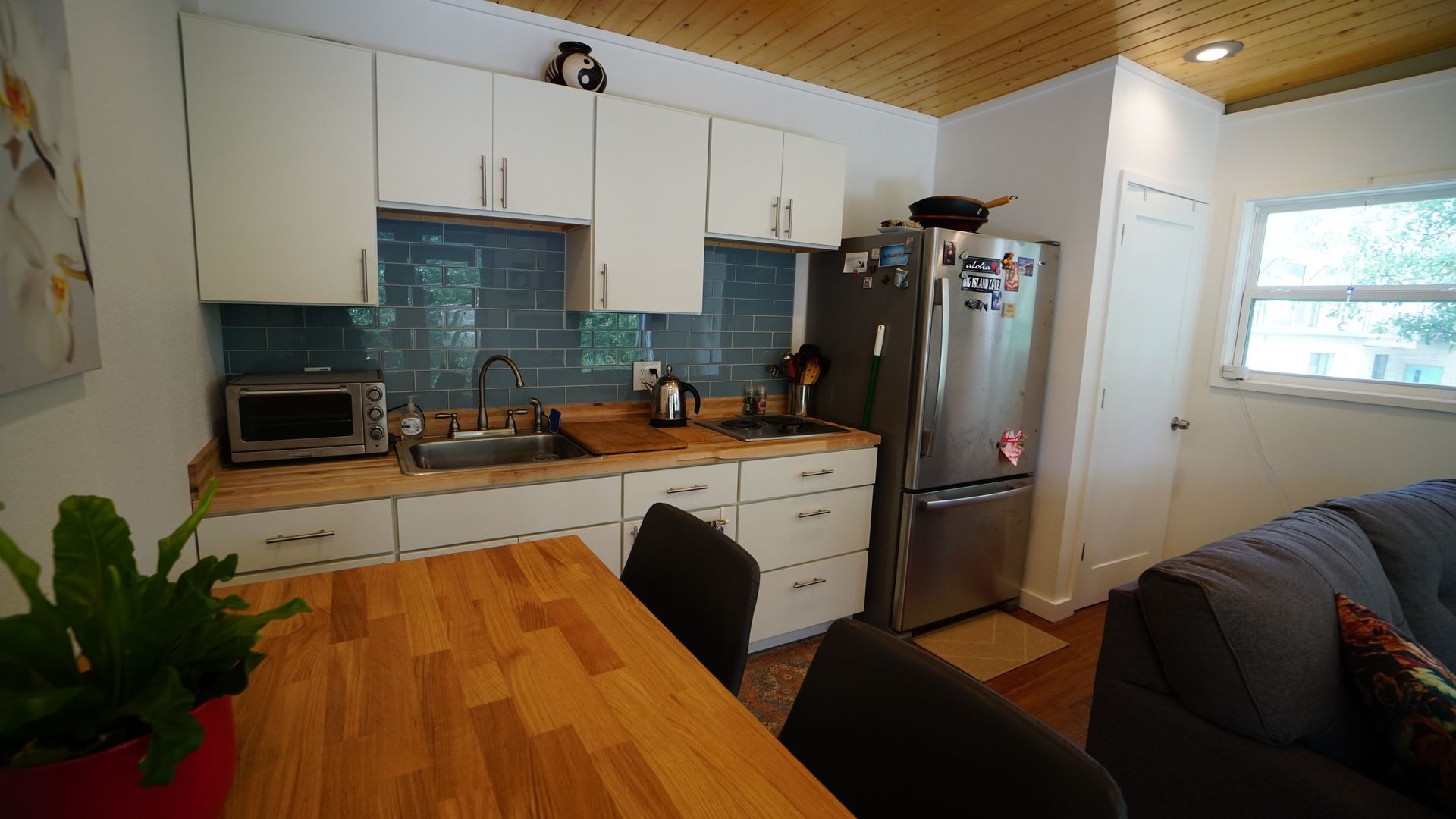 Small kitchen with white cabinets, stainless steel fridge, and wooden table.