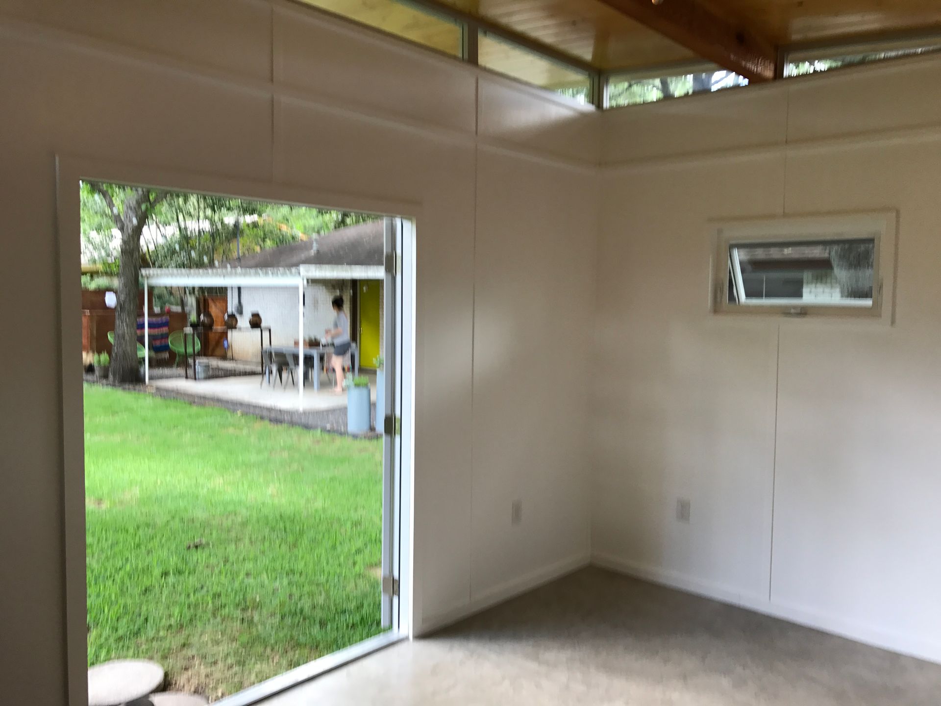Interior of a room with a doorway and window overlooking a backyard with green grass and a patio.