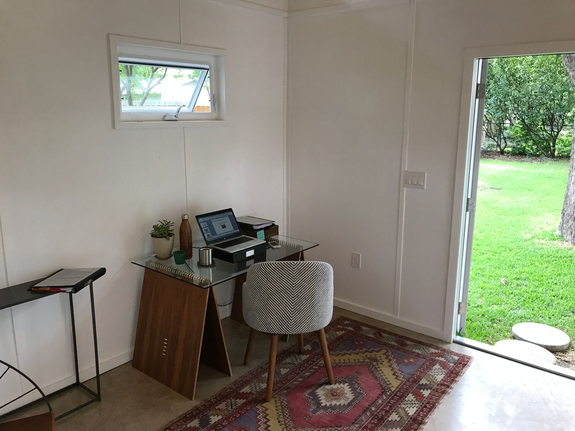 Interior home office with desk, chair, laptop, small window, open door to yard.