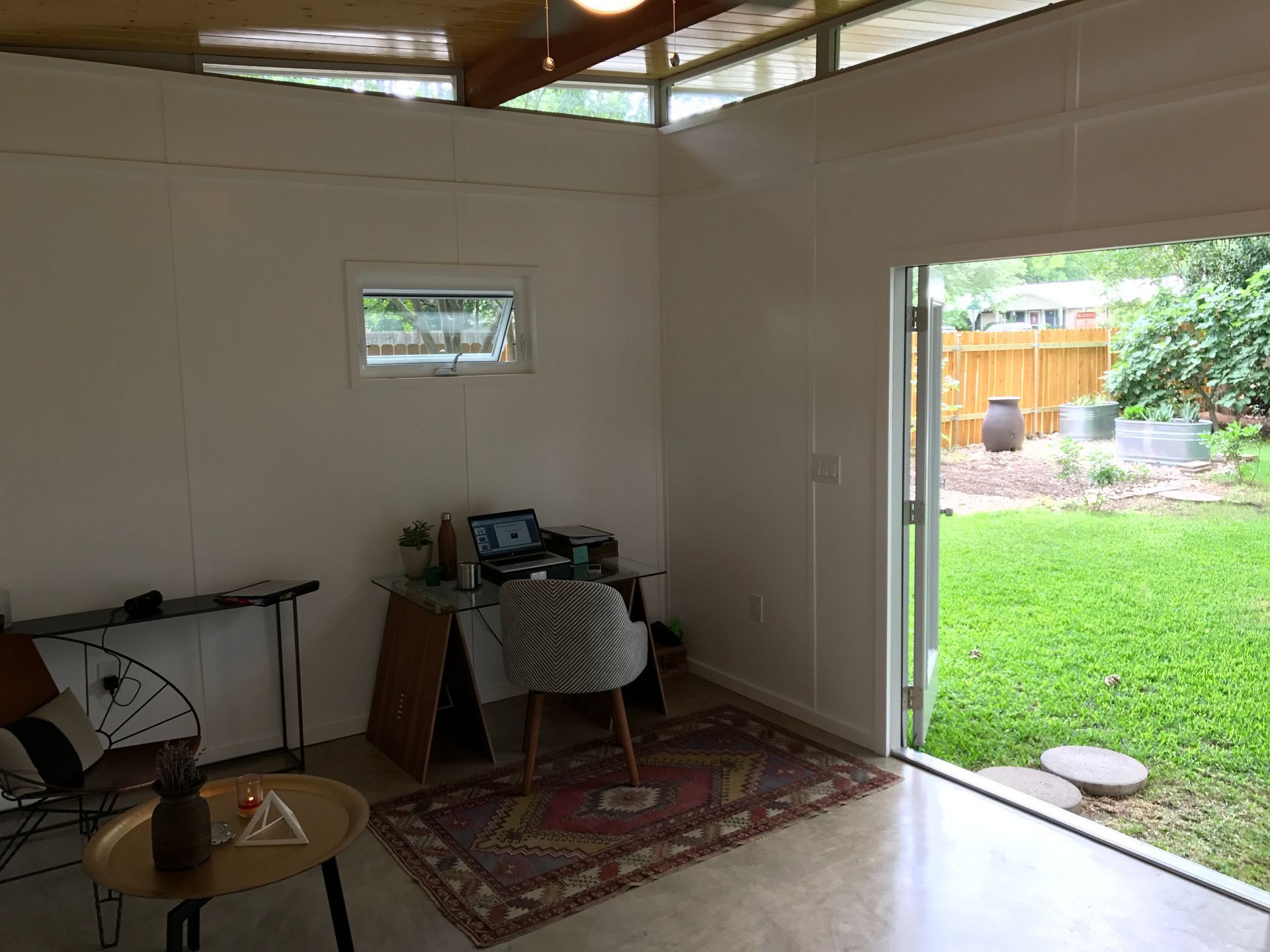 Interior of a small room with an open door to a backyard. Contains a desk, chair, rug, and a small table.