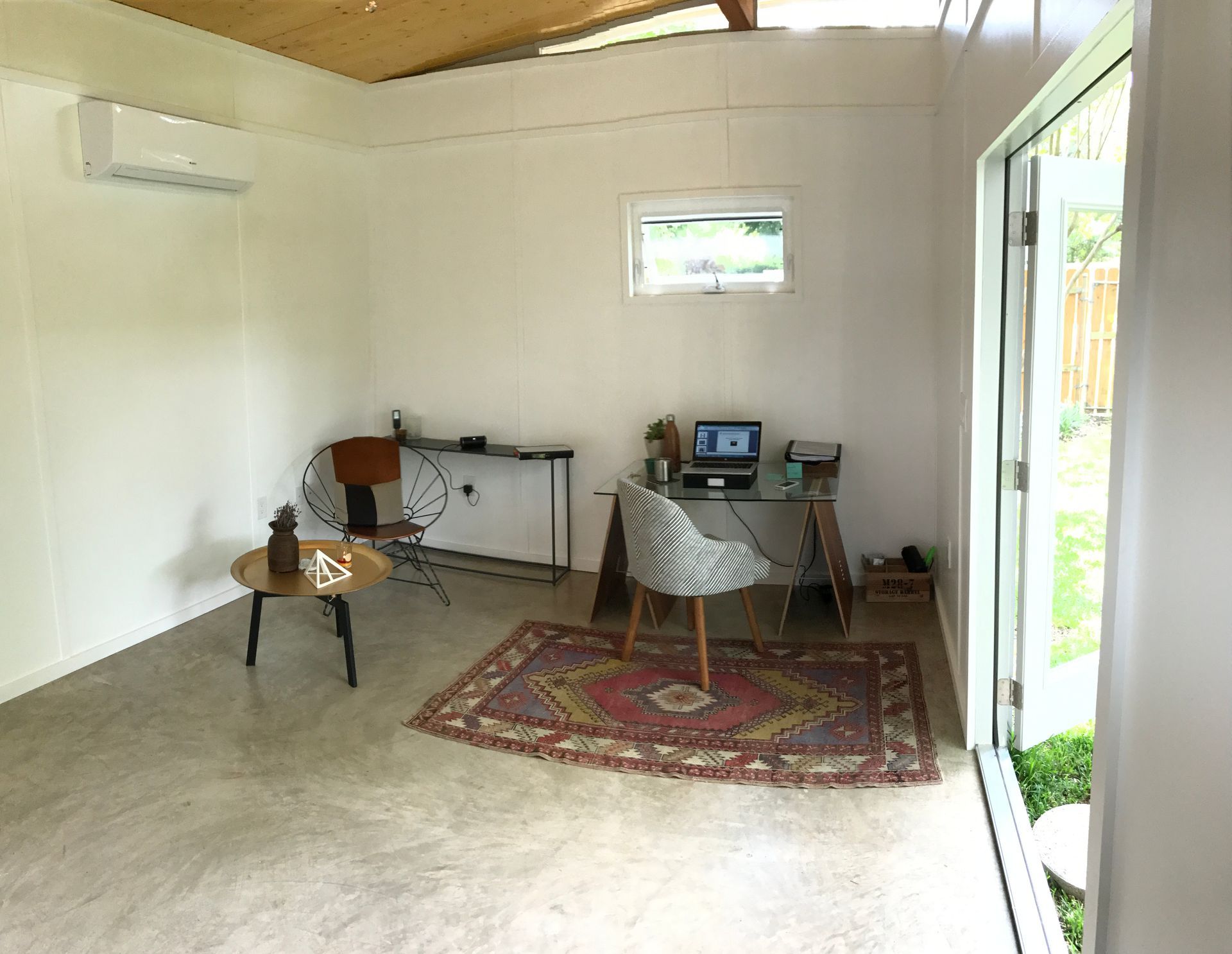Bright interior office space with desk, chair, rug, and open door to a yard.