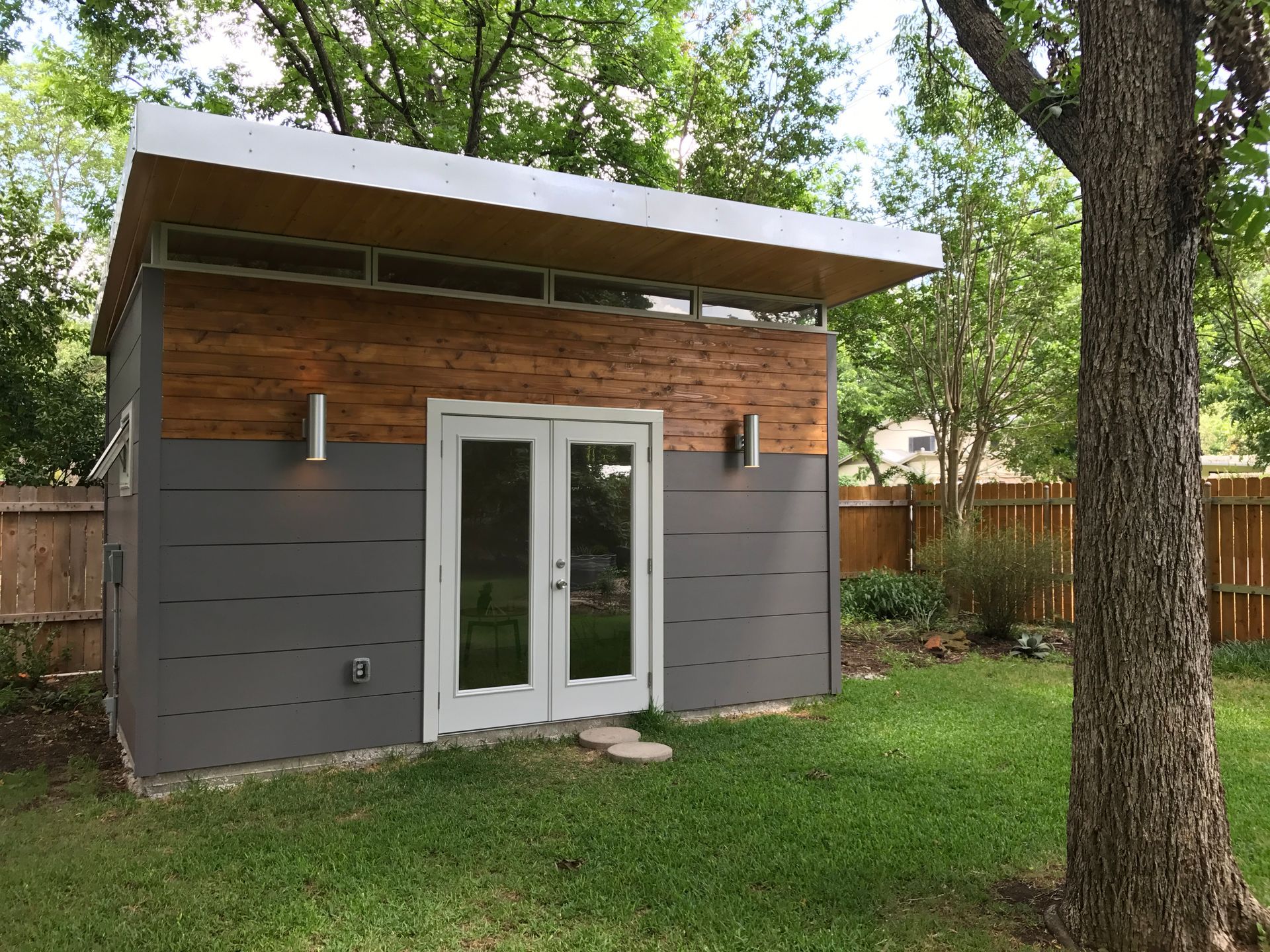 Modern backyard studio with gray siding, wood accent, and double glass doors.