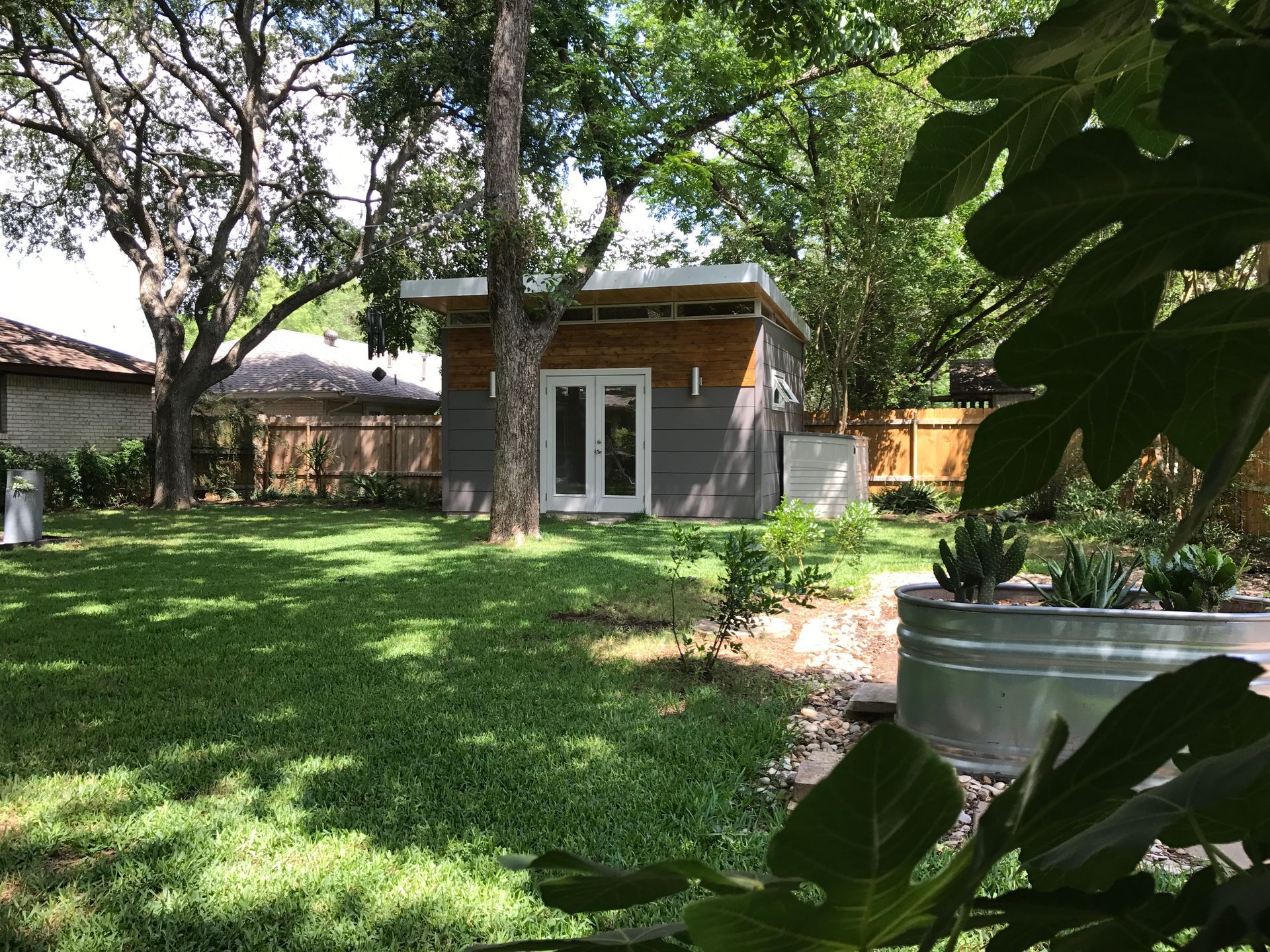 Backyard with a modern shed, grass, trees, and metal planter with succulents.