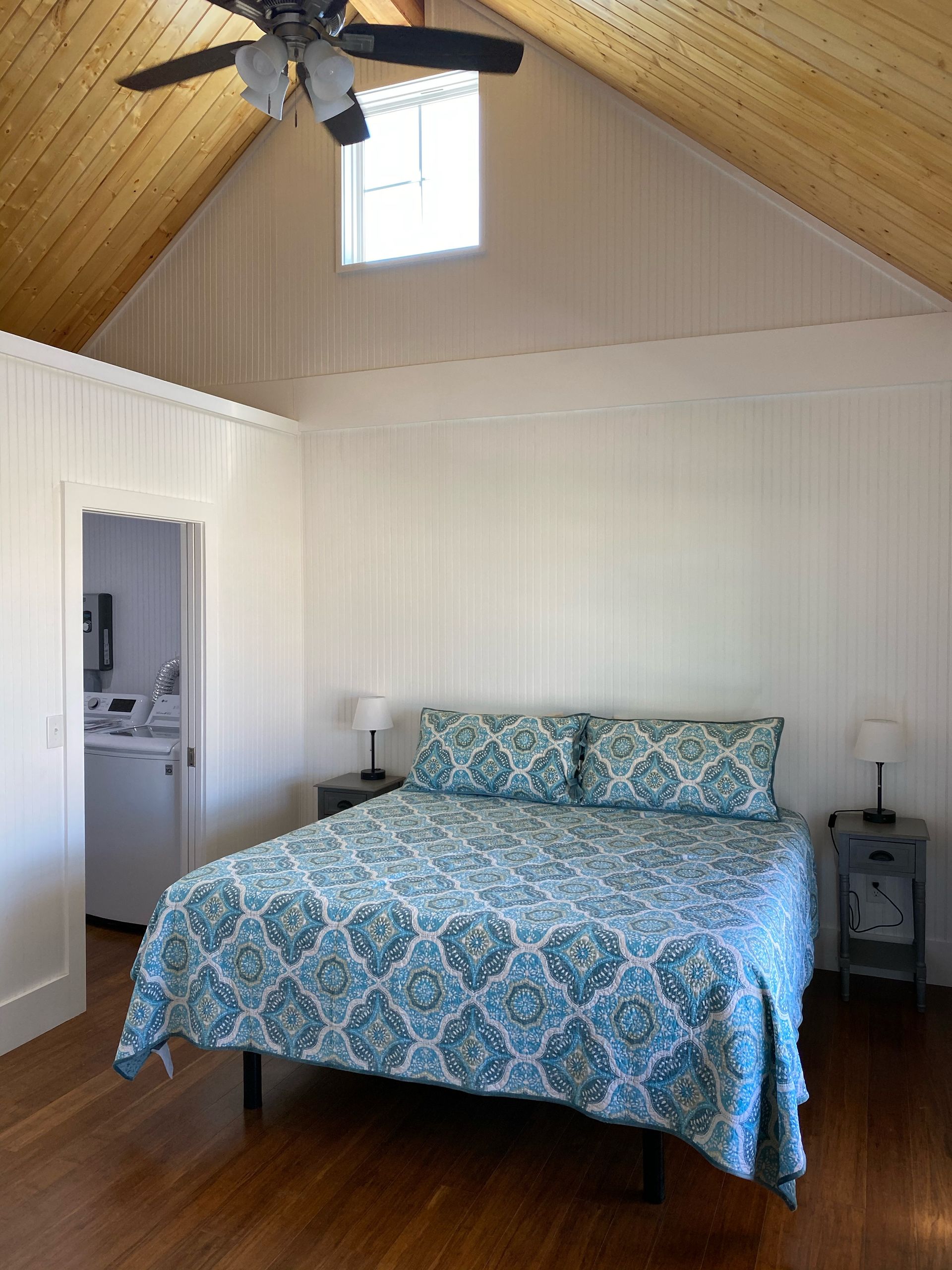 Bedroom with a bed, nightstands, and a door to the left. The ceiling is wood.