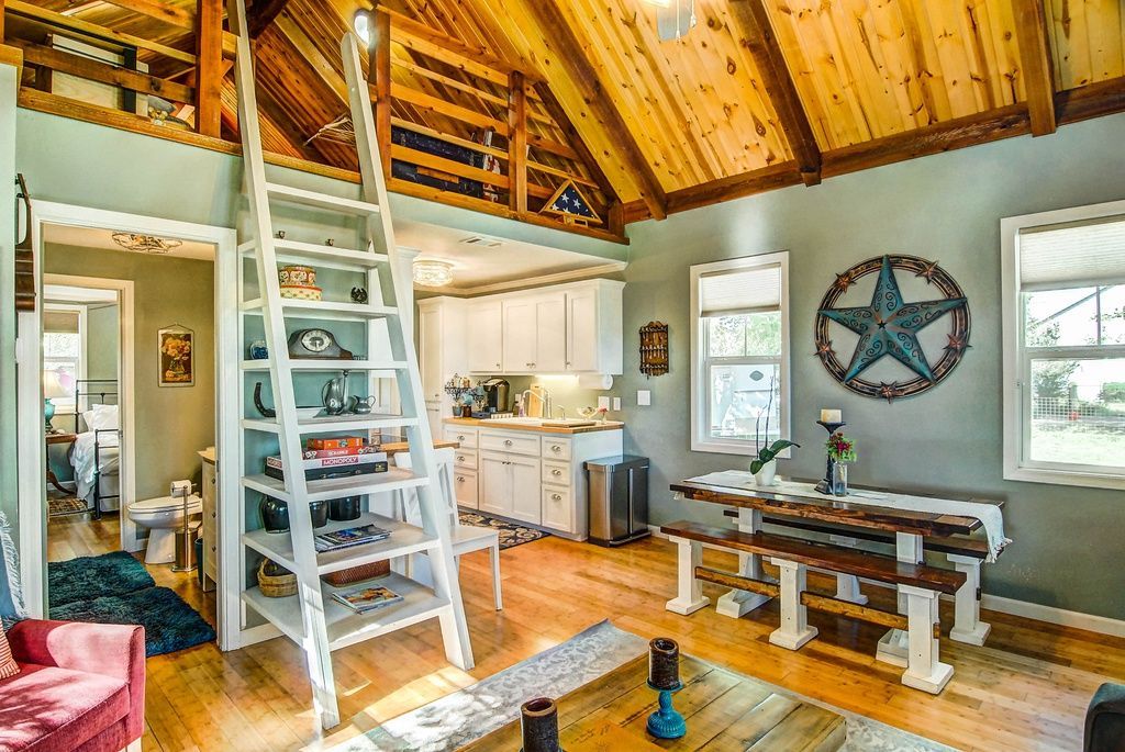 Cozy cabin interior with a ladder to a loft, wooden beams, a dining table, and blue walls.