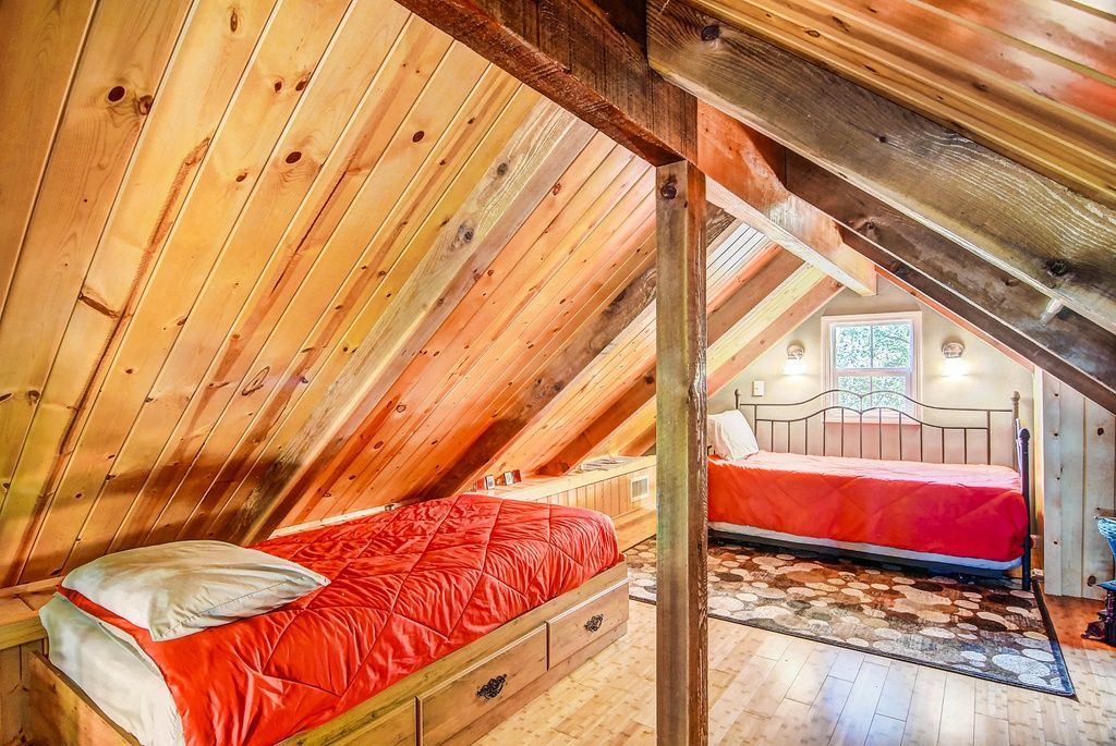 Two beds in a wood-paneled attic bedroom; one with a red comforter, the other with an orange comforter.