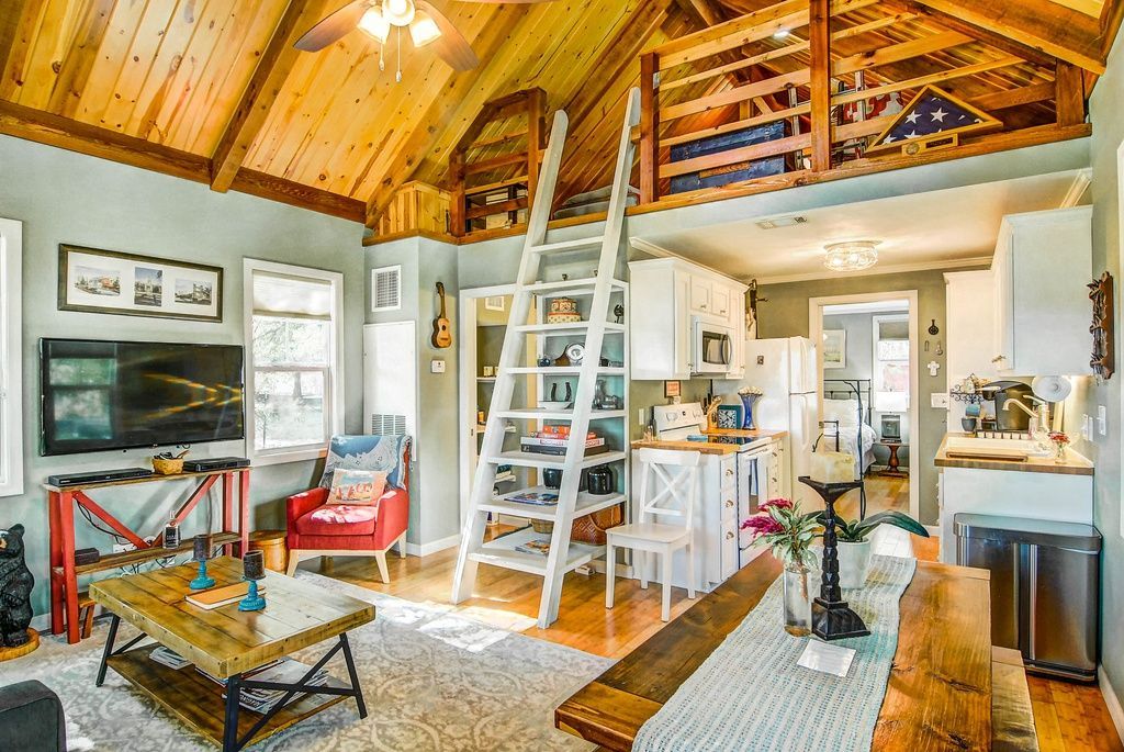 Cozy cabin interior with a loft, wooden beams, ladder, living and dining area.