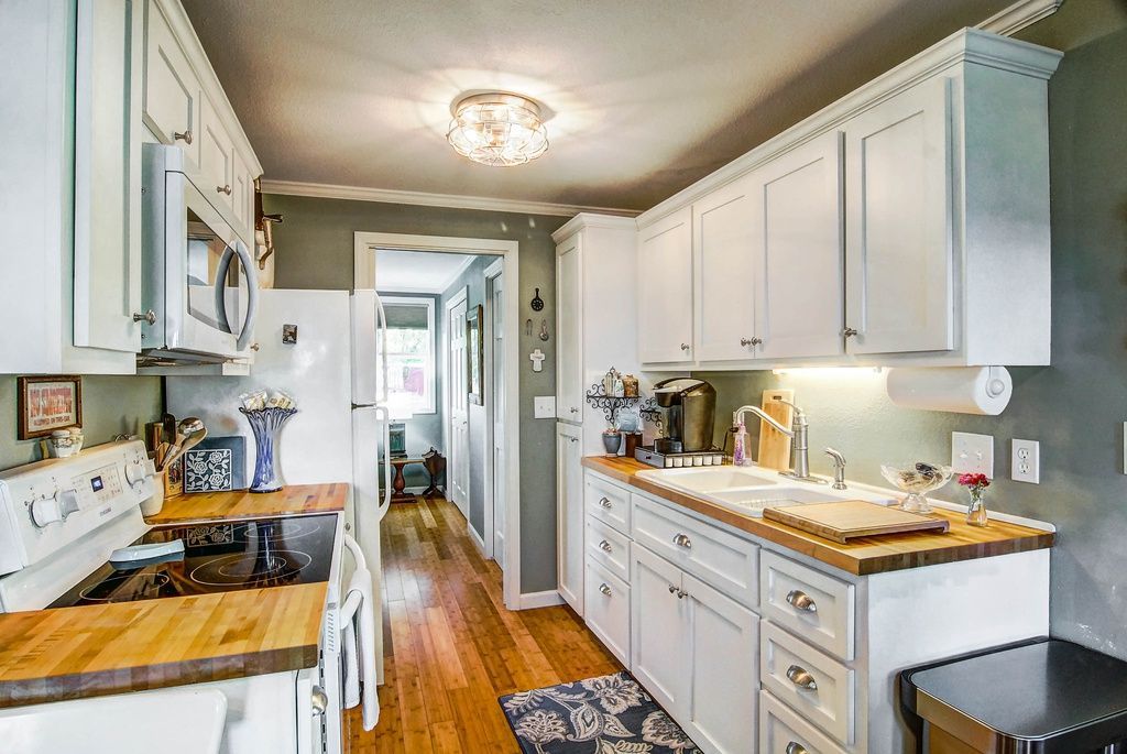 Kitchen with white cabinets, wooden countertops, and a view into a hallway.