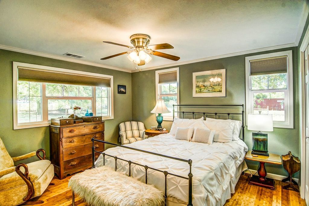 Bedroom with bed, dresser, seating, and windows; green walls, natural light.
