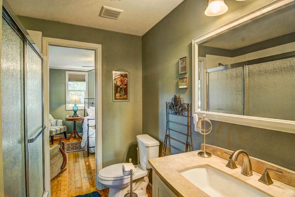 Bathroom with sage green walls, sink, toilet, mirror, and doorway leading to a bedroom.