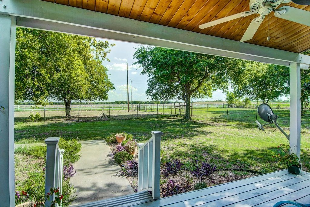 View from a porch overlooking a grassy yard, trees, and a distant body of water.