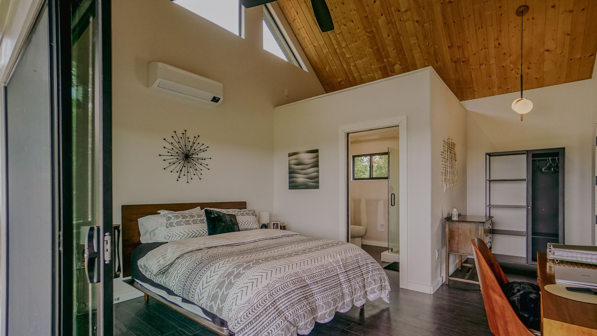 Bedroom with bed, bathroom doorway, window, and wood ceiling.
