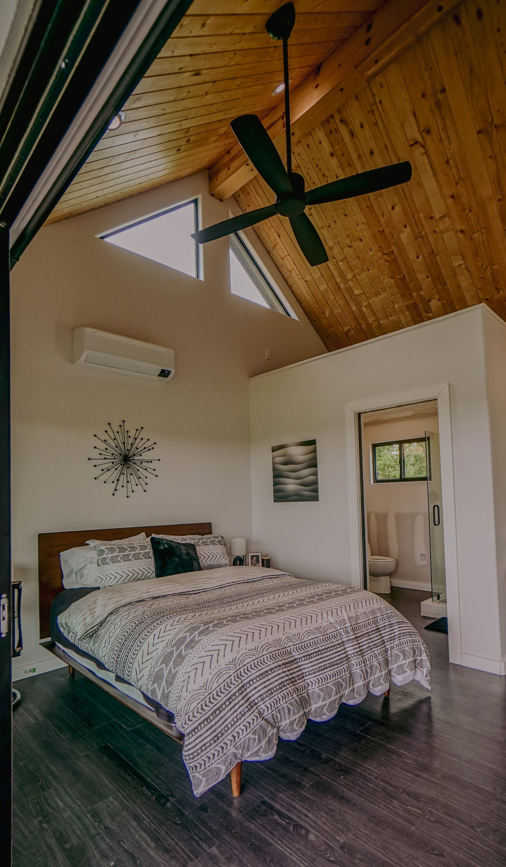 Bedroom with wood ceiling, bed, fan, and open doorway to bathroom.
