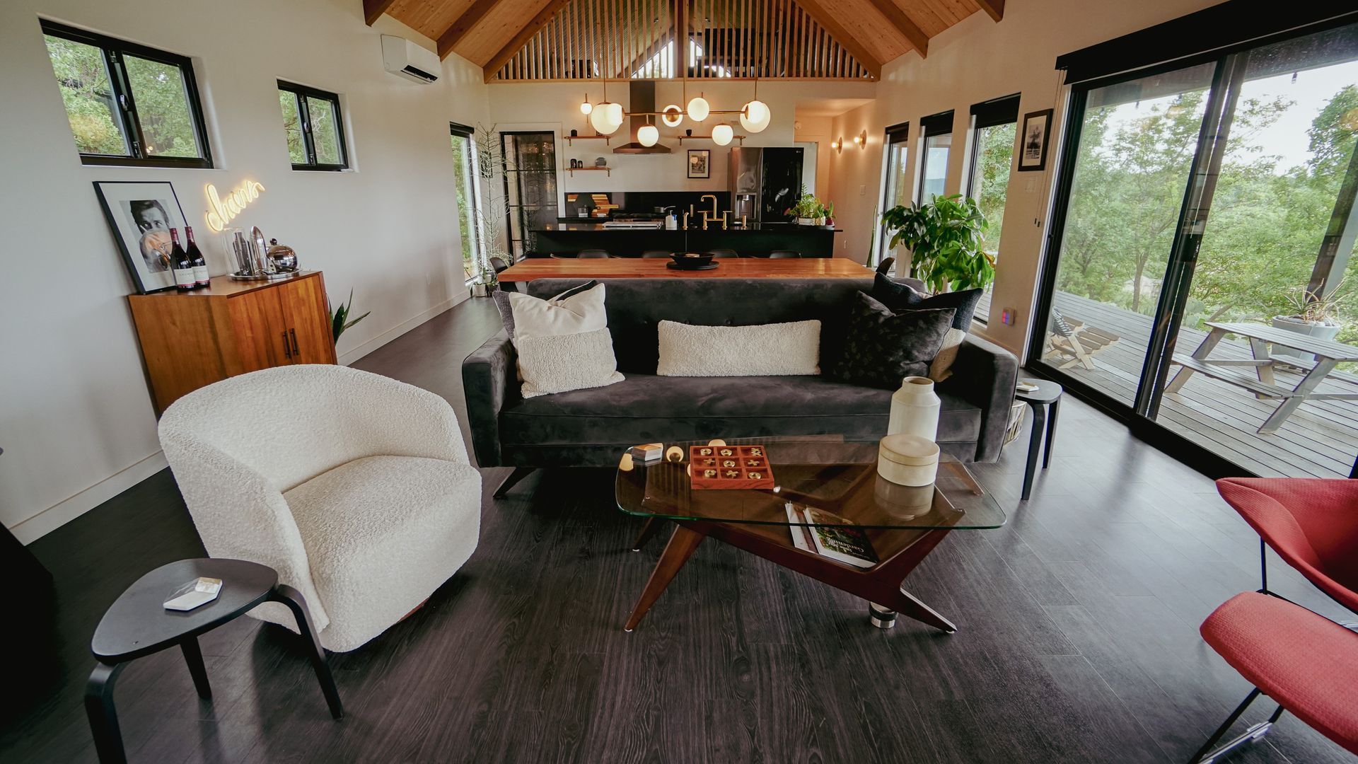 Living room with dark gray sofa, white armchair, glass coffee table, and dark wooden floor.