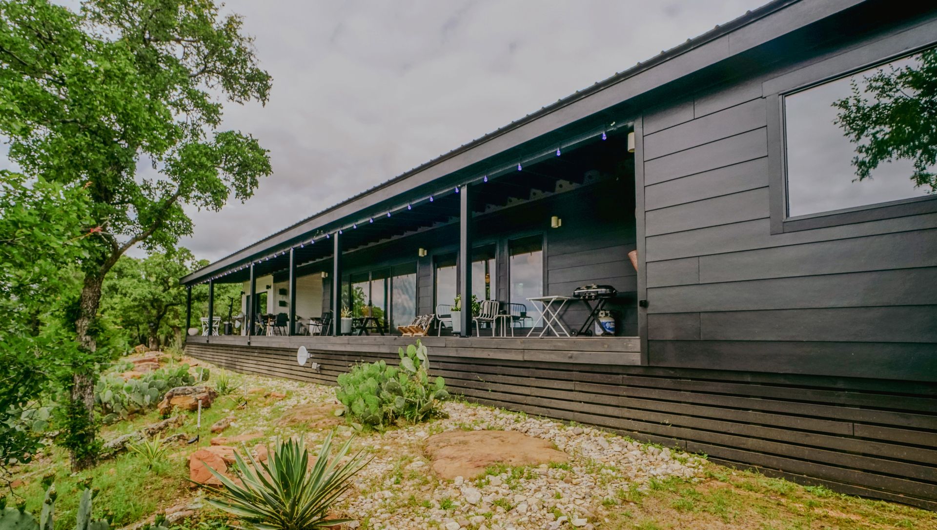 Long, modern home with a dark exterior, covered porch, and large windows on a hillside.