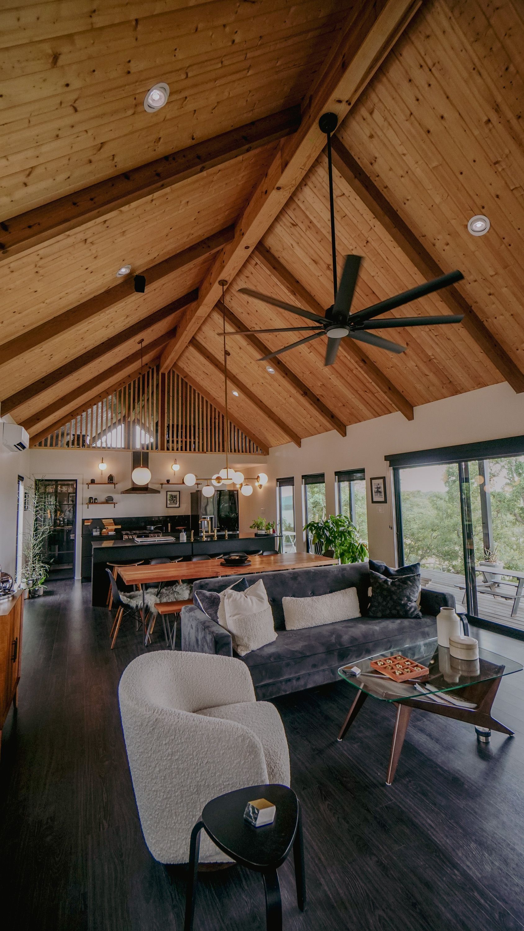 Living room with wood-paneled vaulted ceiling, dark wood floors, large sofa, armchairs, and dining area.