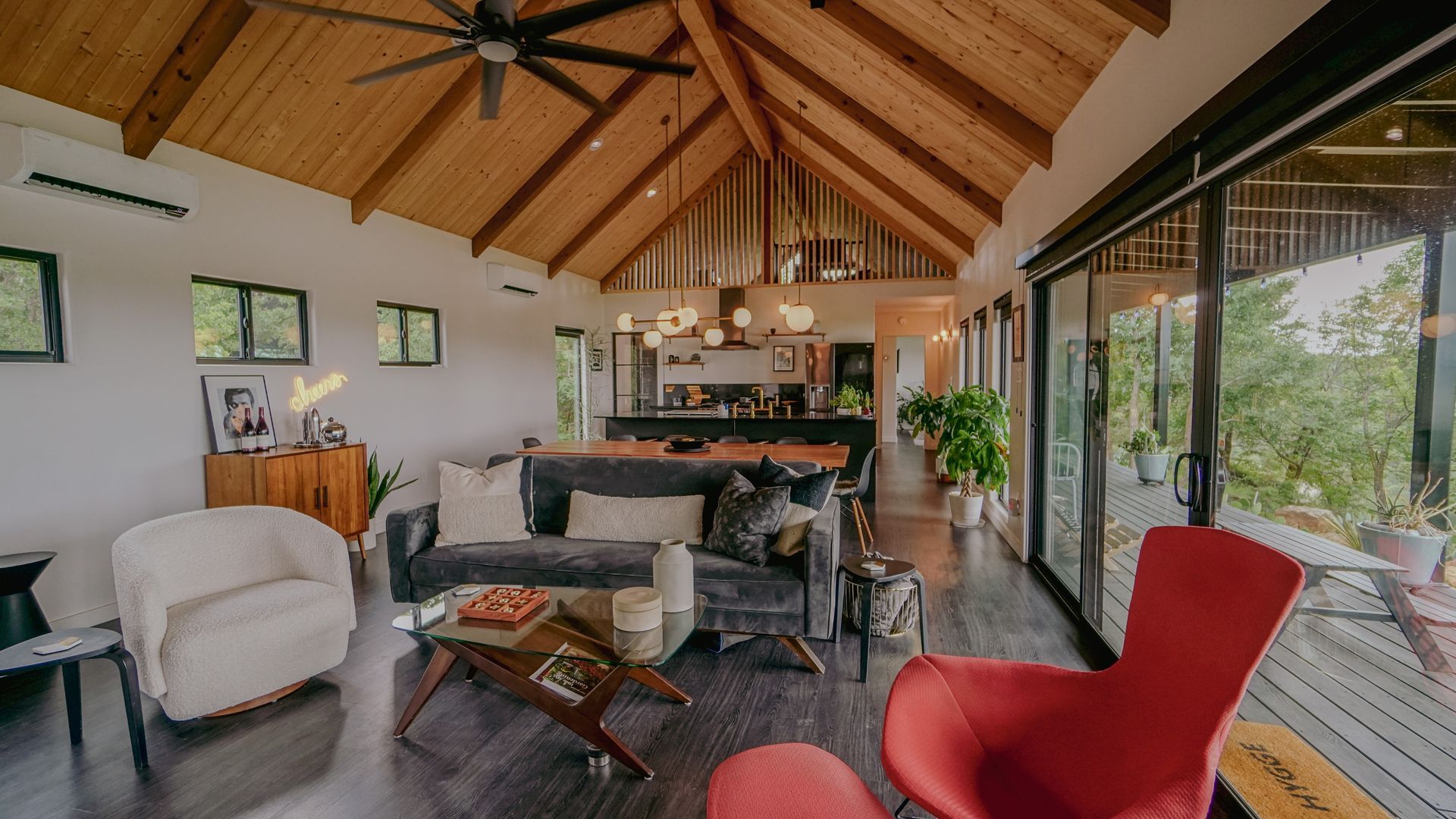 Spacious living room with vaulted wood ceiling, dark floors, and large windows overlooking a deck.