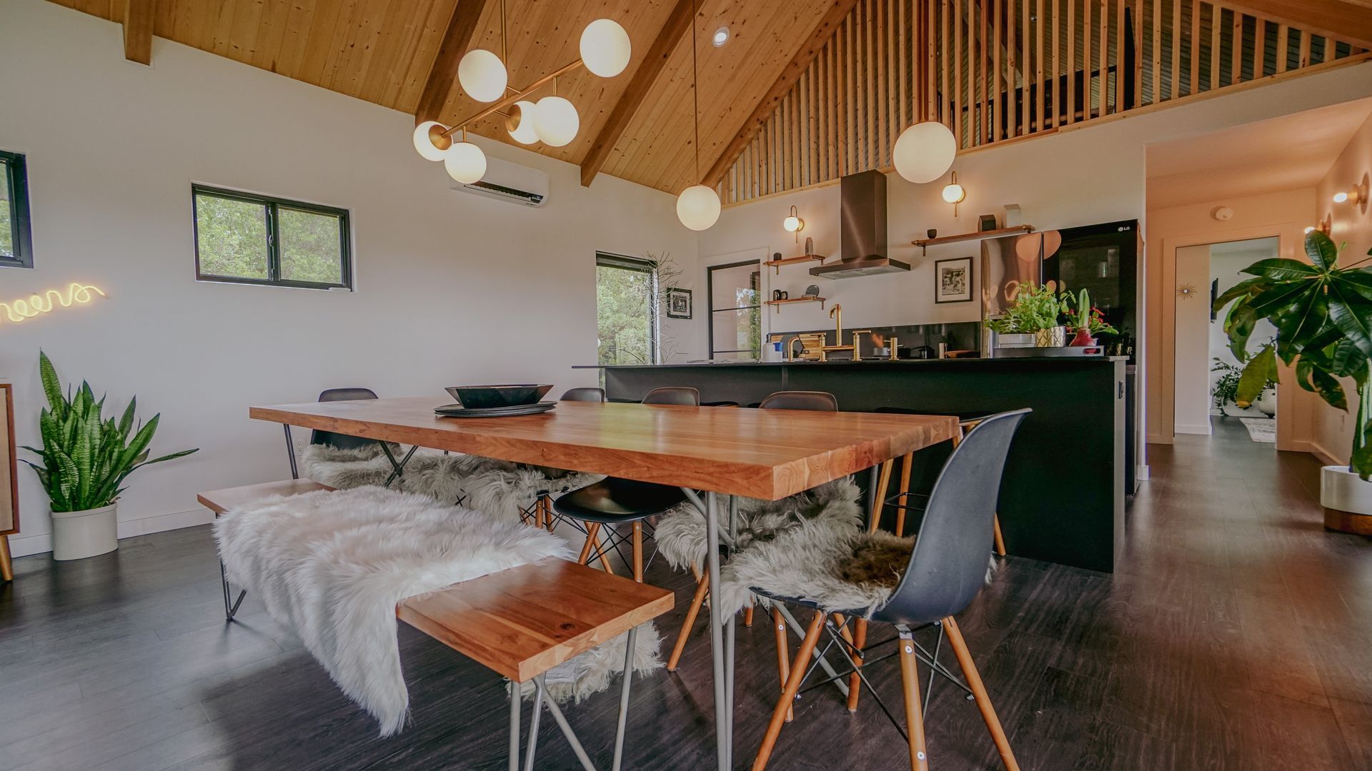 Dining area with wooden table, benches with sheepskin throws, black chairs, and globe lights.