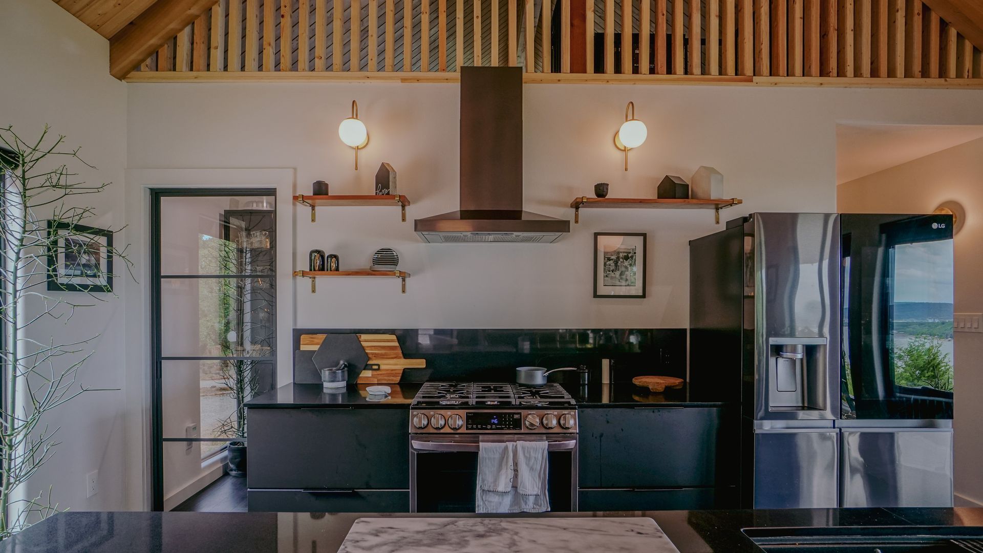 Modern kitchen with black cabinets, stainless steel appliances, copper range hood, and wood shelving.