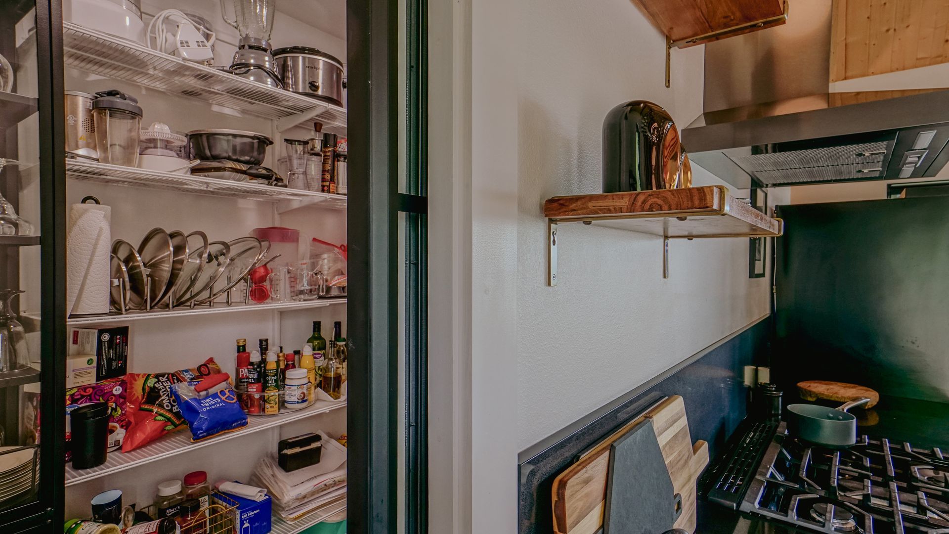 Kitchen pantry overflowing with food and appliances, open doorway to cooking area.